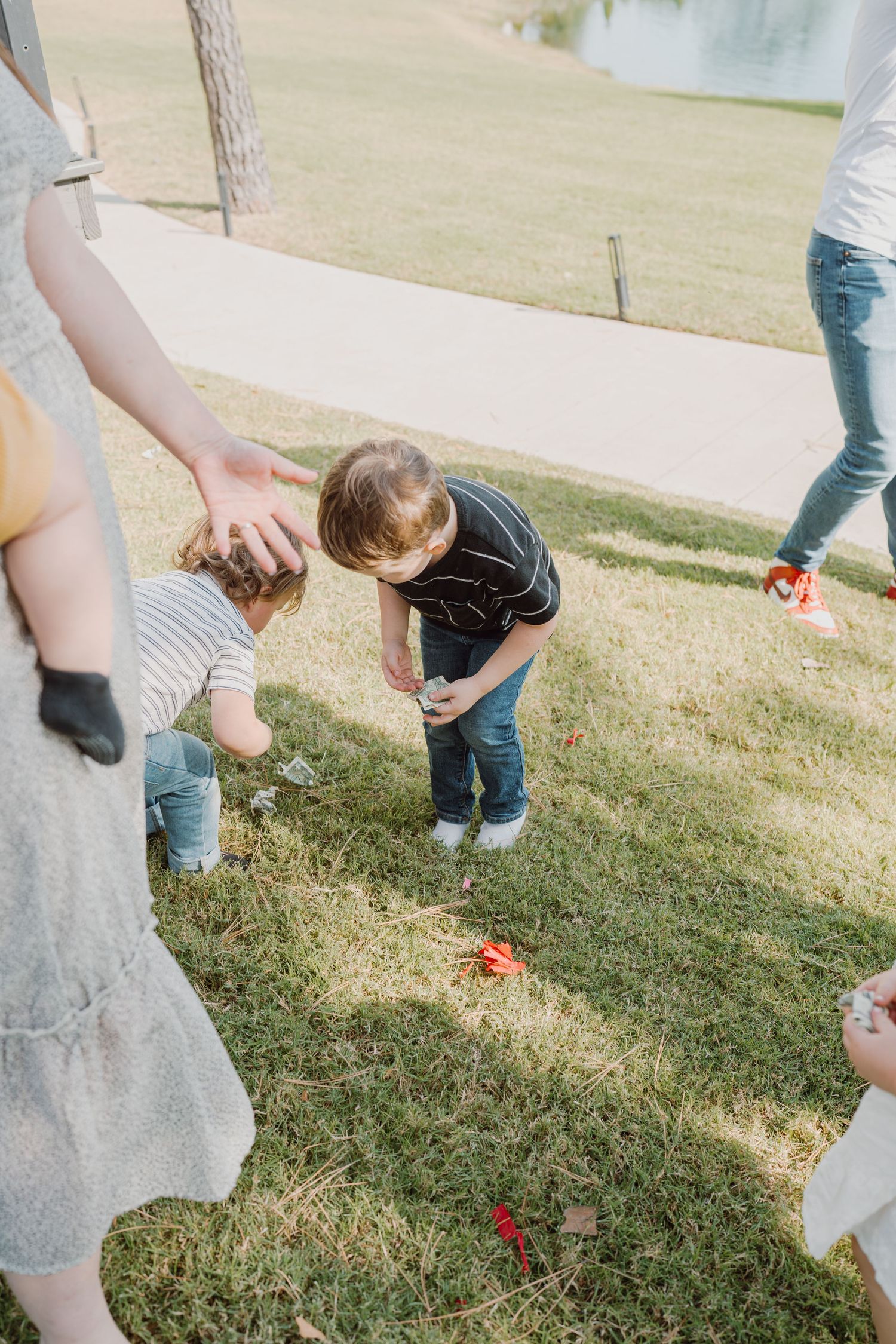 People gather around to collect items falling from a broken piñata on grass.