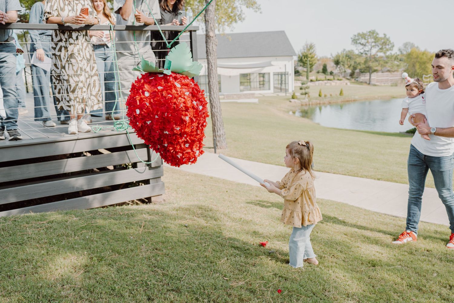 A large red heart decoration swings between people on a grassy slope near houses.