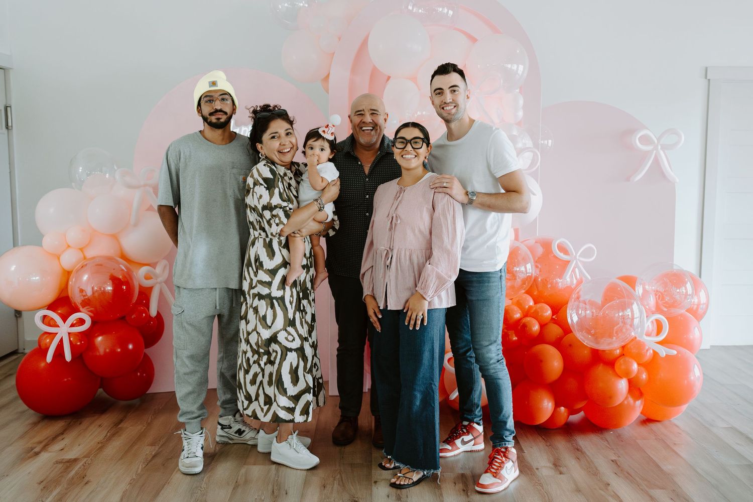 Birthday party scene with coral balloon arch and 'Happy Birthday' sign in bright studio setting.