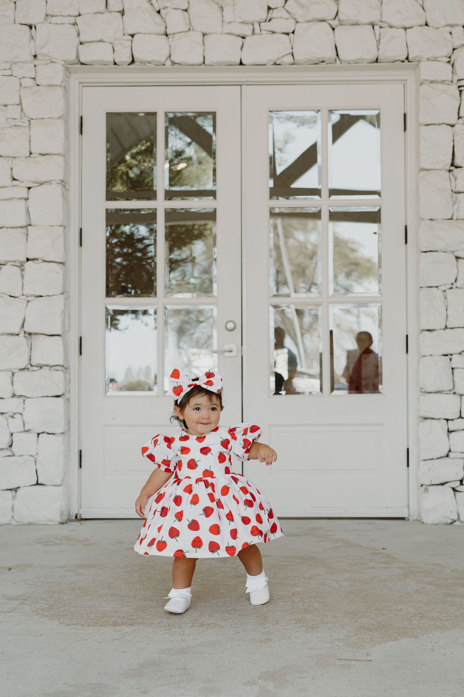 Small child in heart-patterned dress and bow crawling near white doors.