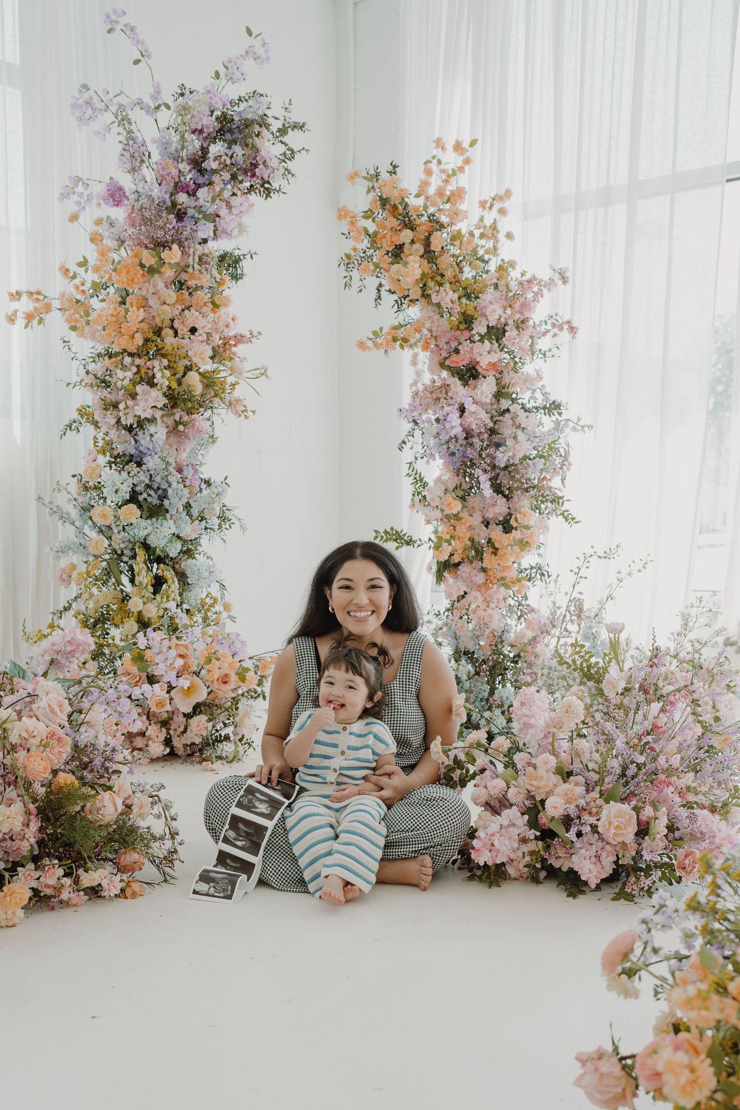 Studio photography session with soft lighting and elegant floral decorations in pastel colors.