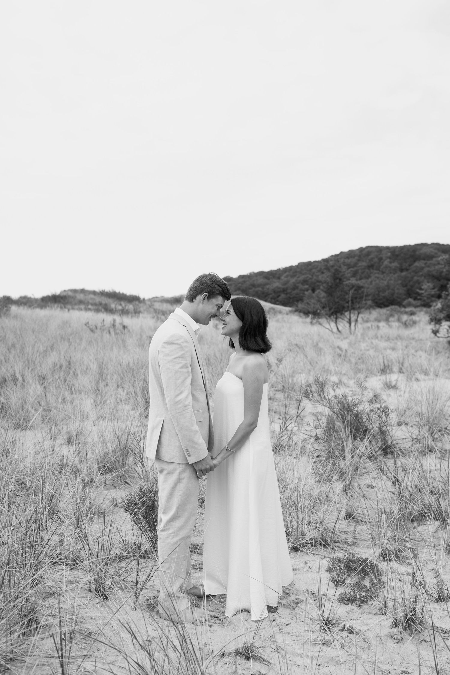 Black and white image of a couple sharing an intimate moment on sandy dunes.
