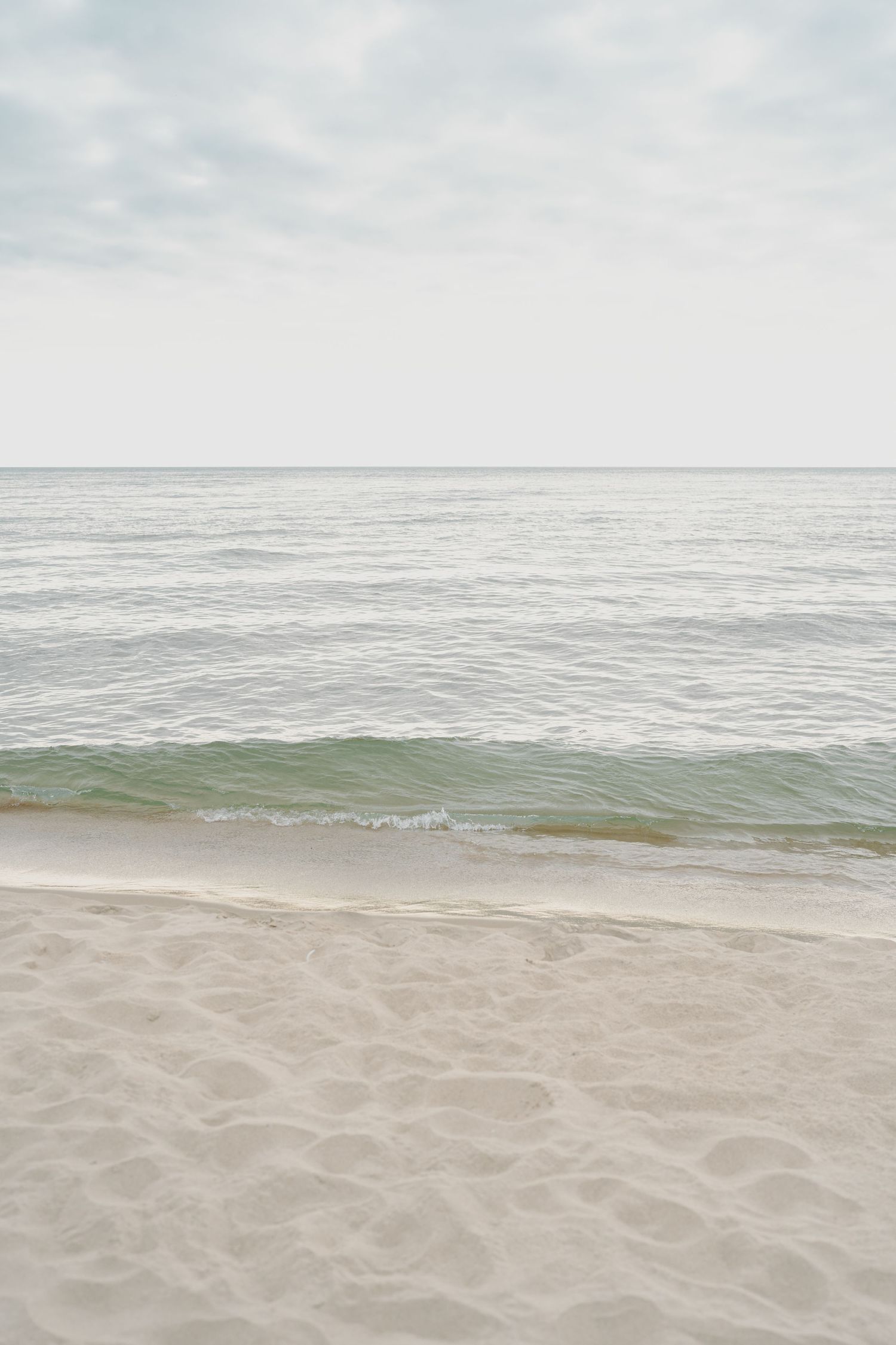 Serene ocean landscape with gentle waves meeting sandy shore under cloudy sky.