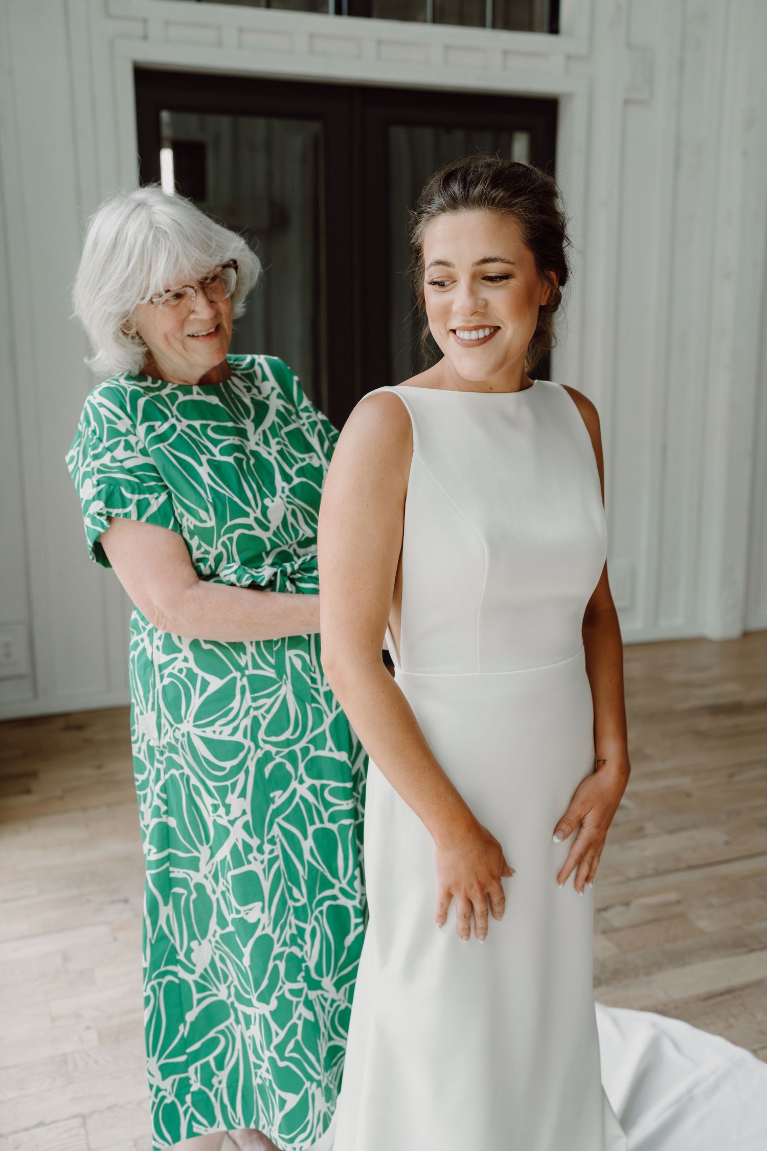 Joyful embrace shared between two people, one in white bridal gown and another in green floral dress.