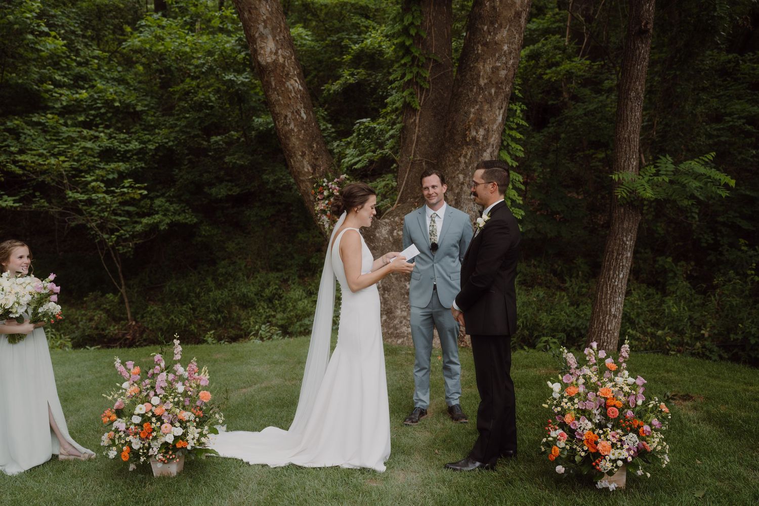 Wedding party gathered in wooded area with beautiful floral arrangements and natural scenery.
