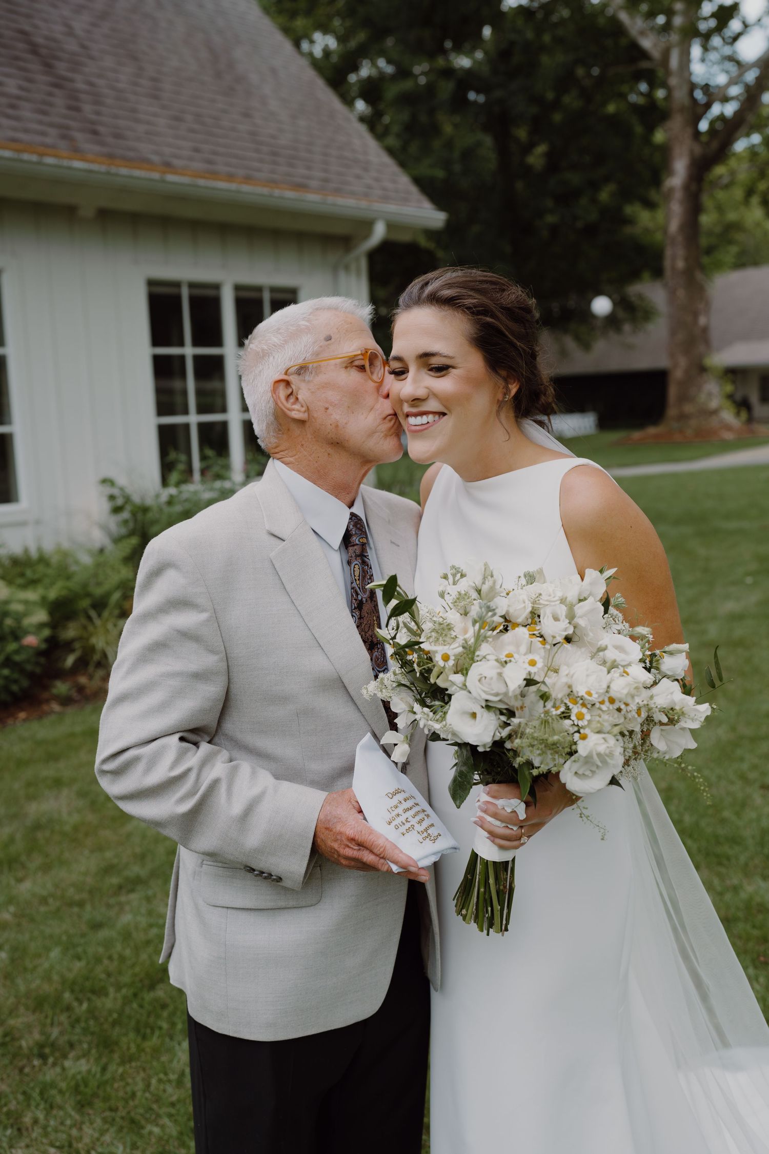 An emotional wedding scene outdoors with white flowers and elegant attire against a natural backdrop.
