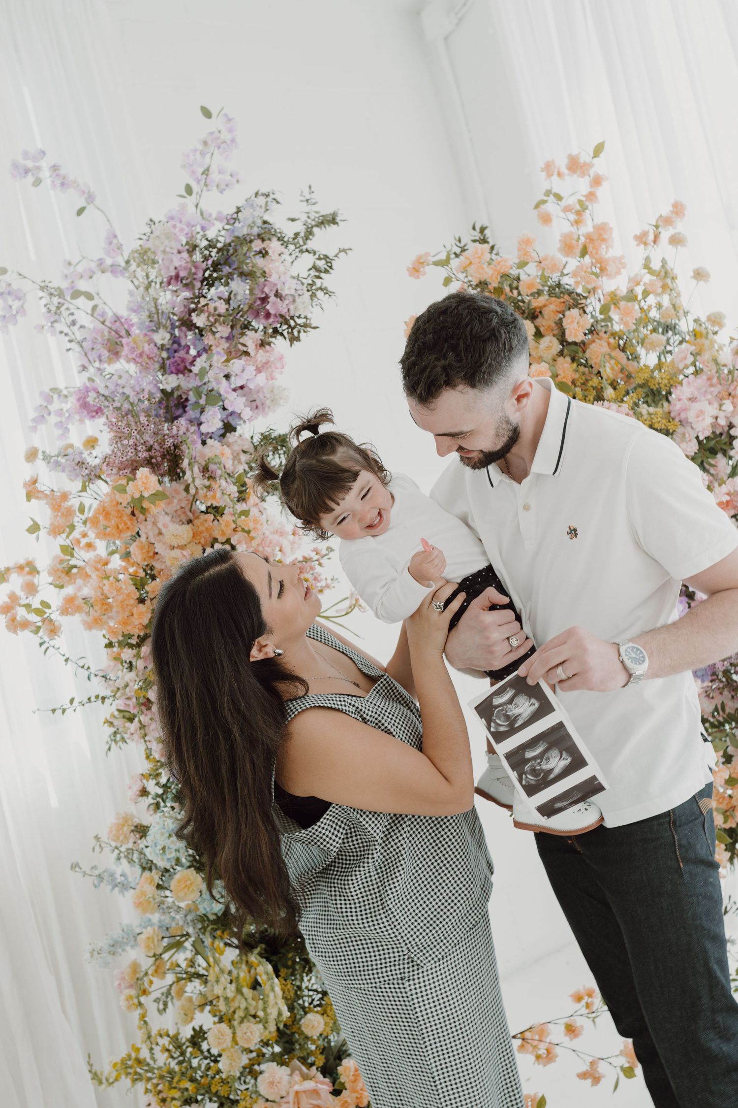 A family shares a joyful moment surrounded by pastel floral arrangements.