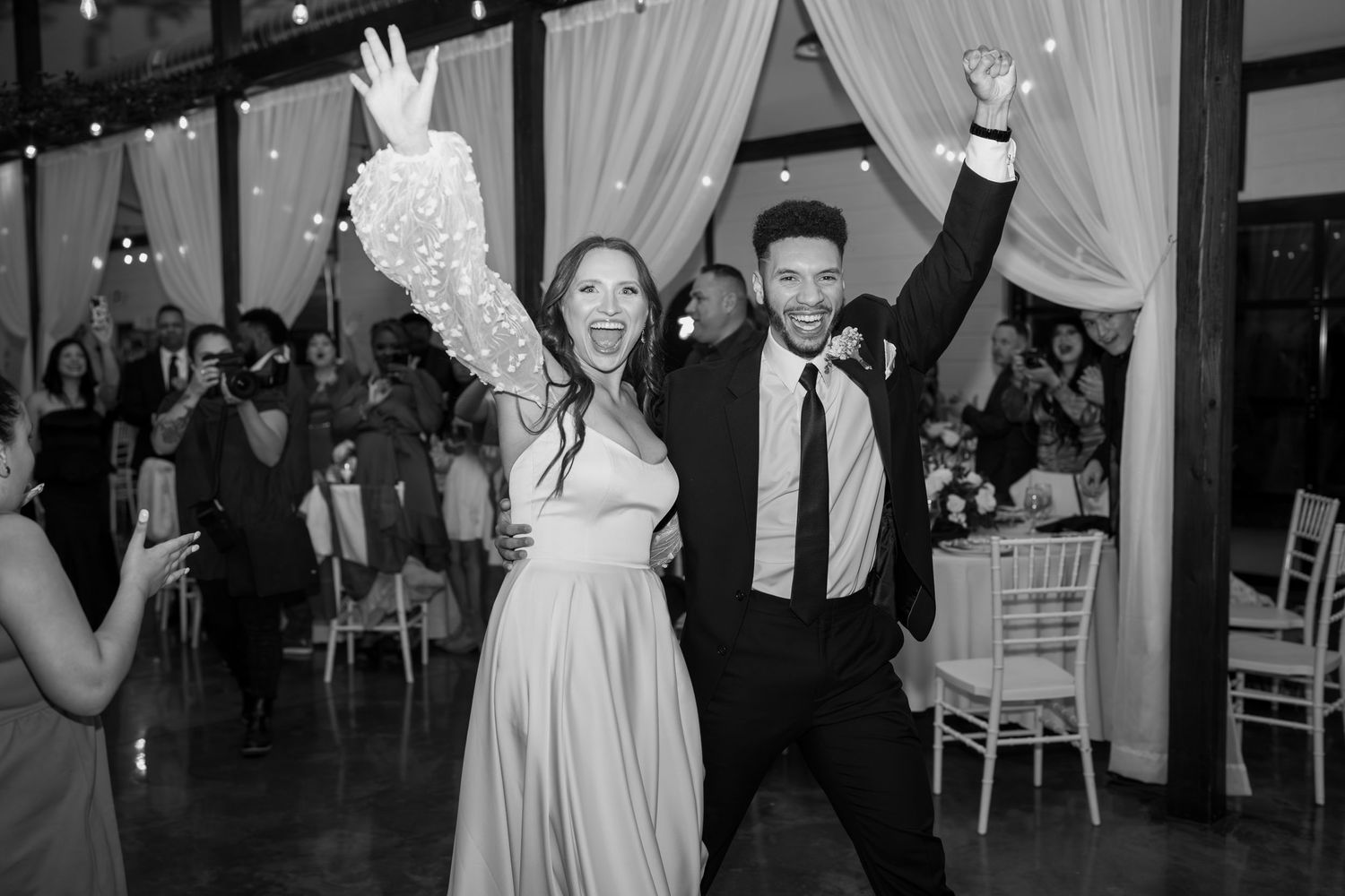 Wedding reception celebration with guests dancing under elegant draped fabric and twinkling lights.