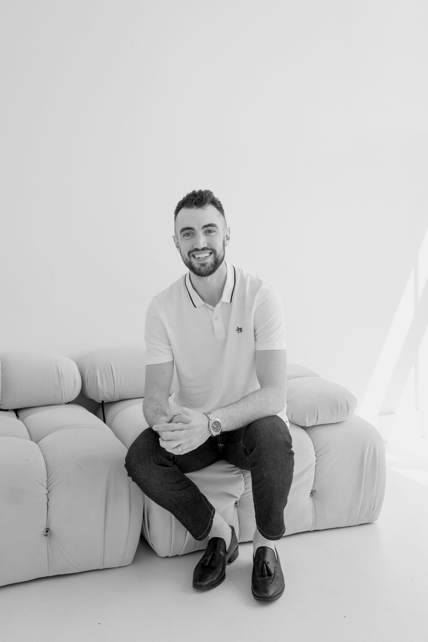 Black and white portraits showing relaxed poses on white furniture in minimalist setting.
