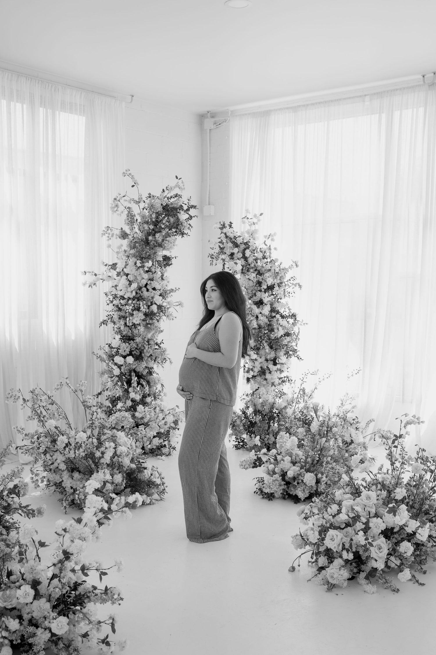 Black and white maternity portrait with elegant floral arrangements creating depth.