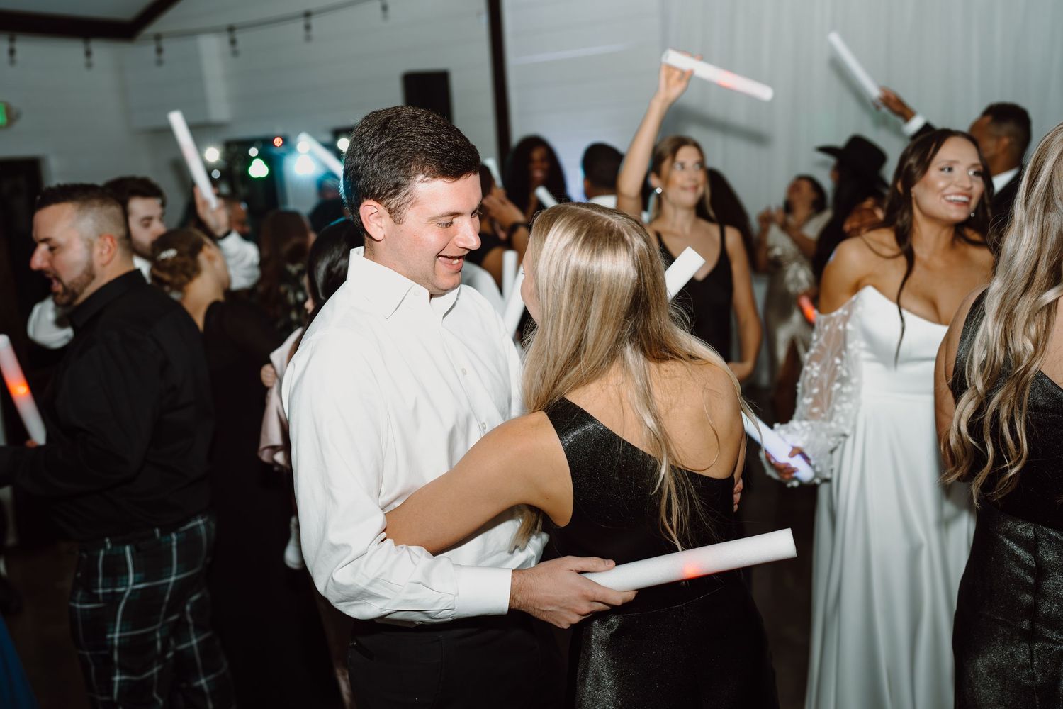 Wedding guests dance with LED foam sticks during an energetic reception celebration.