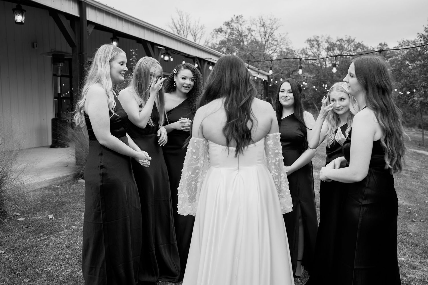 Black and white candid moment of wedding party sharing laughs outside venue.