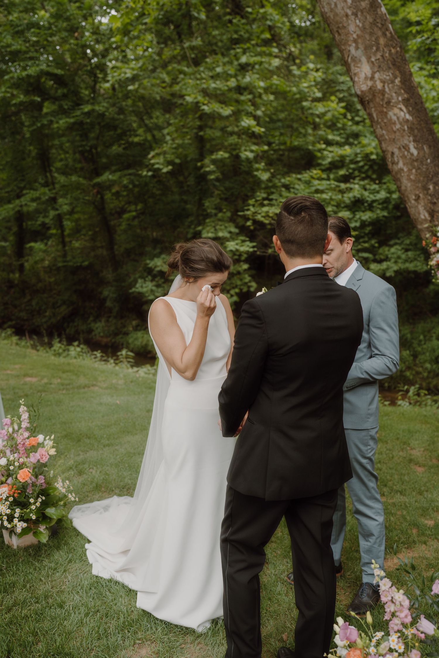 An emotional wedding ceremony moment captured in a green outdoor garden setting.