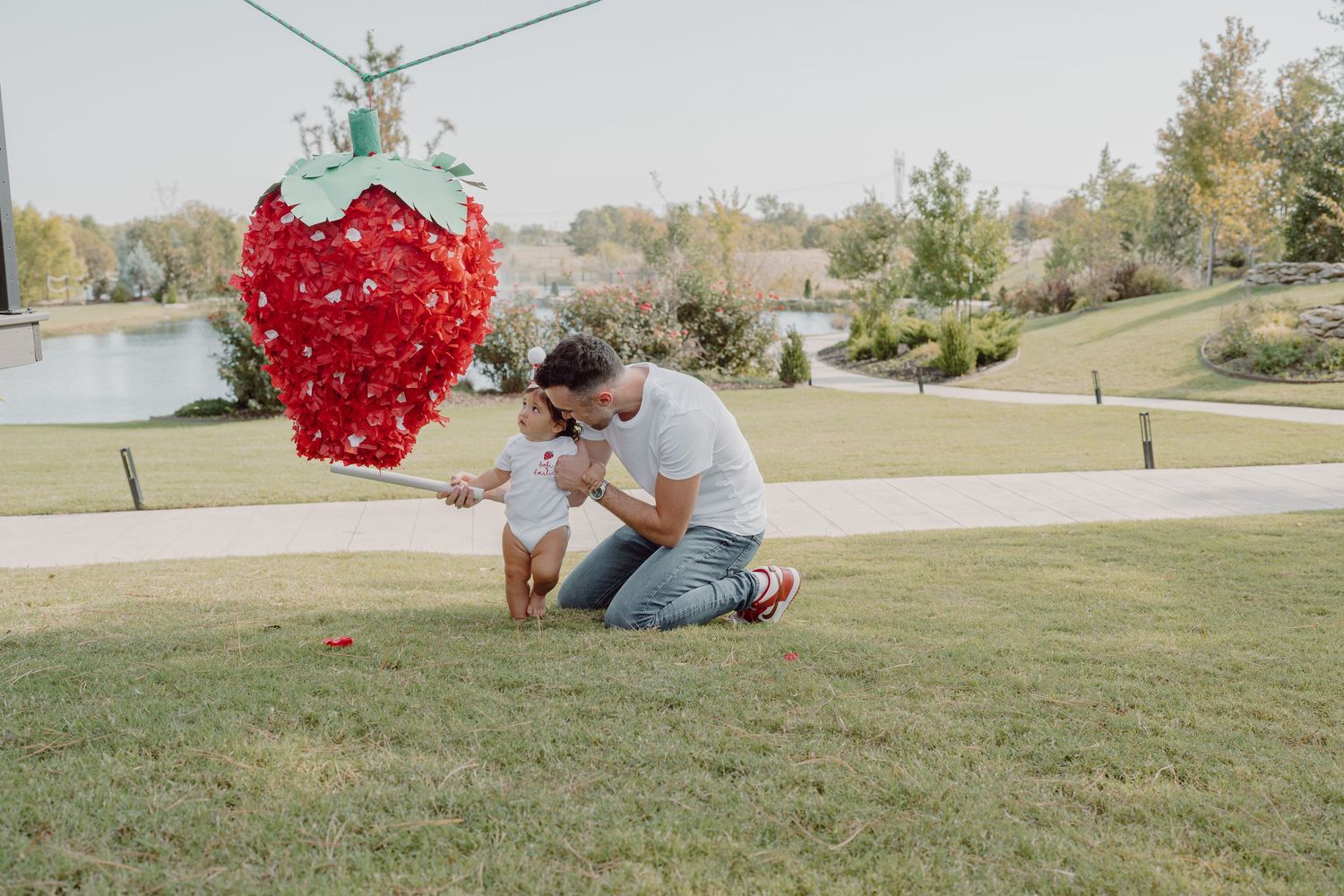 A large decorative red heart swings on a string across a sunny outdoor landscape.