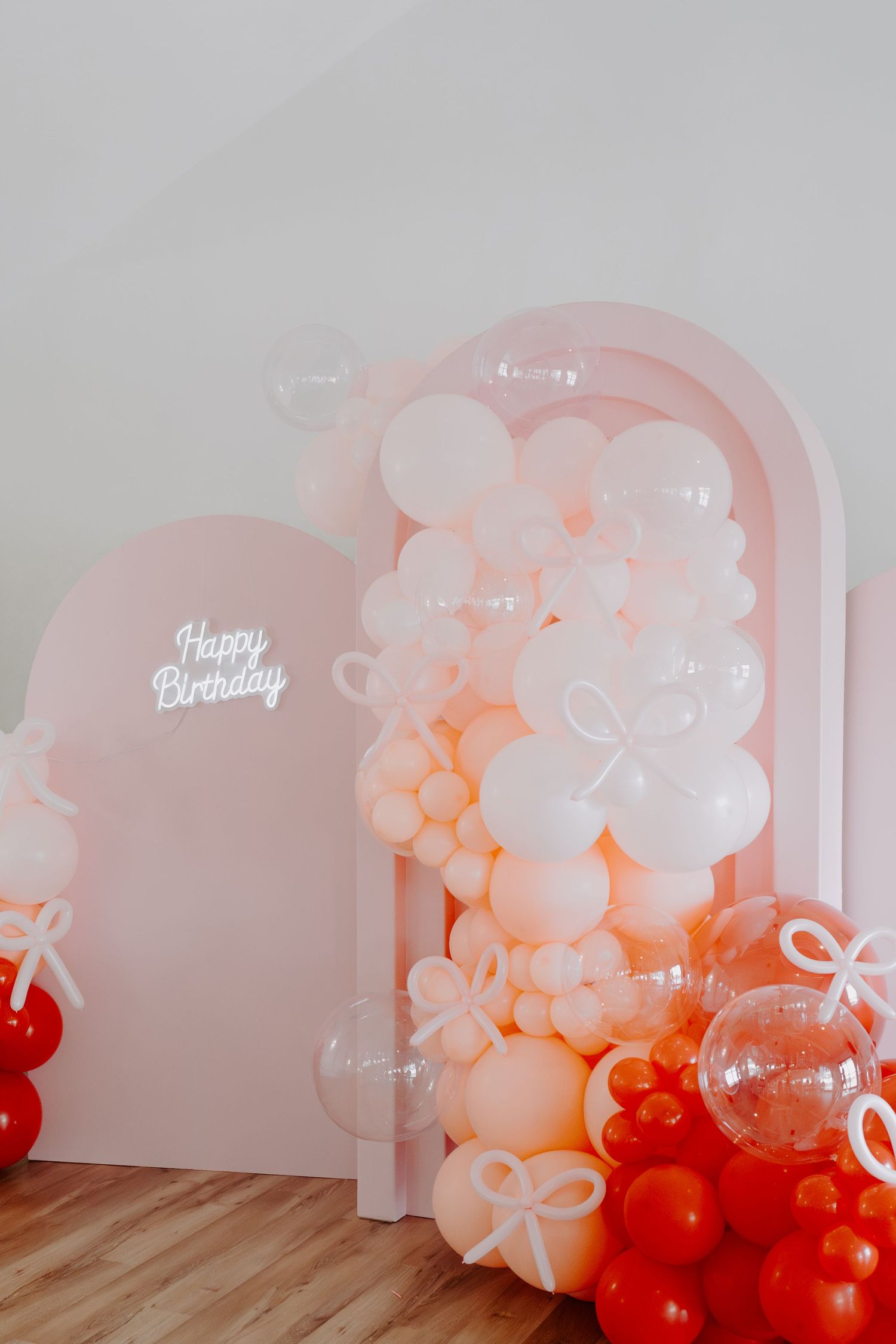 Birthday party setup with ombre balloon garland in coral and white tones against a white backdrop.