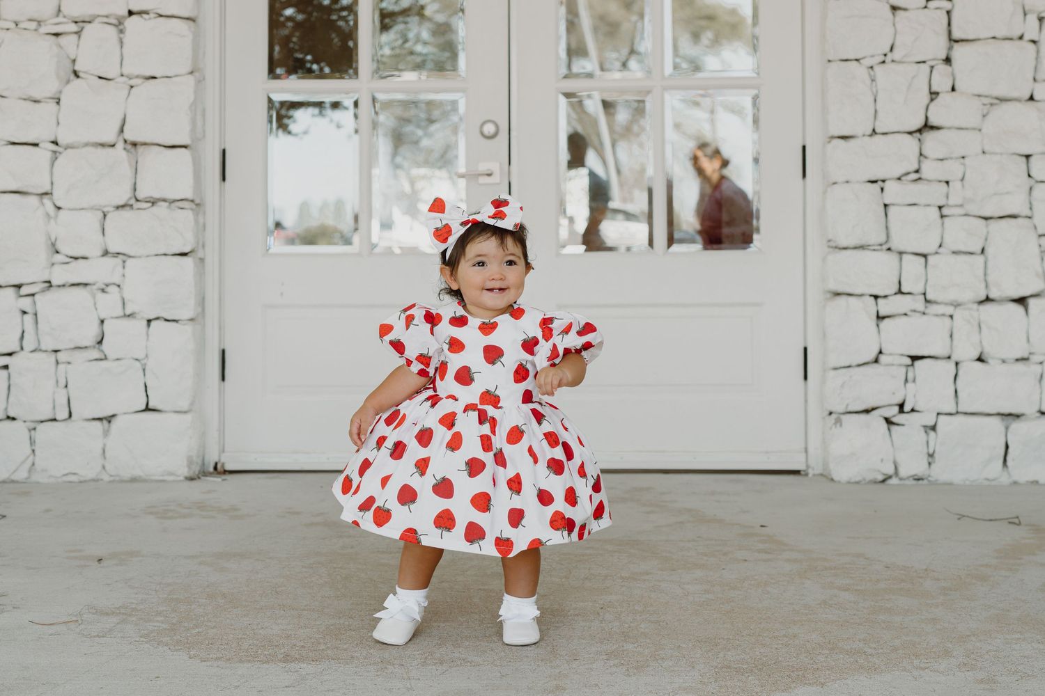 Dancing and twirling in a red heart-patterned dress against white stone backdrop.