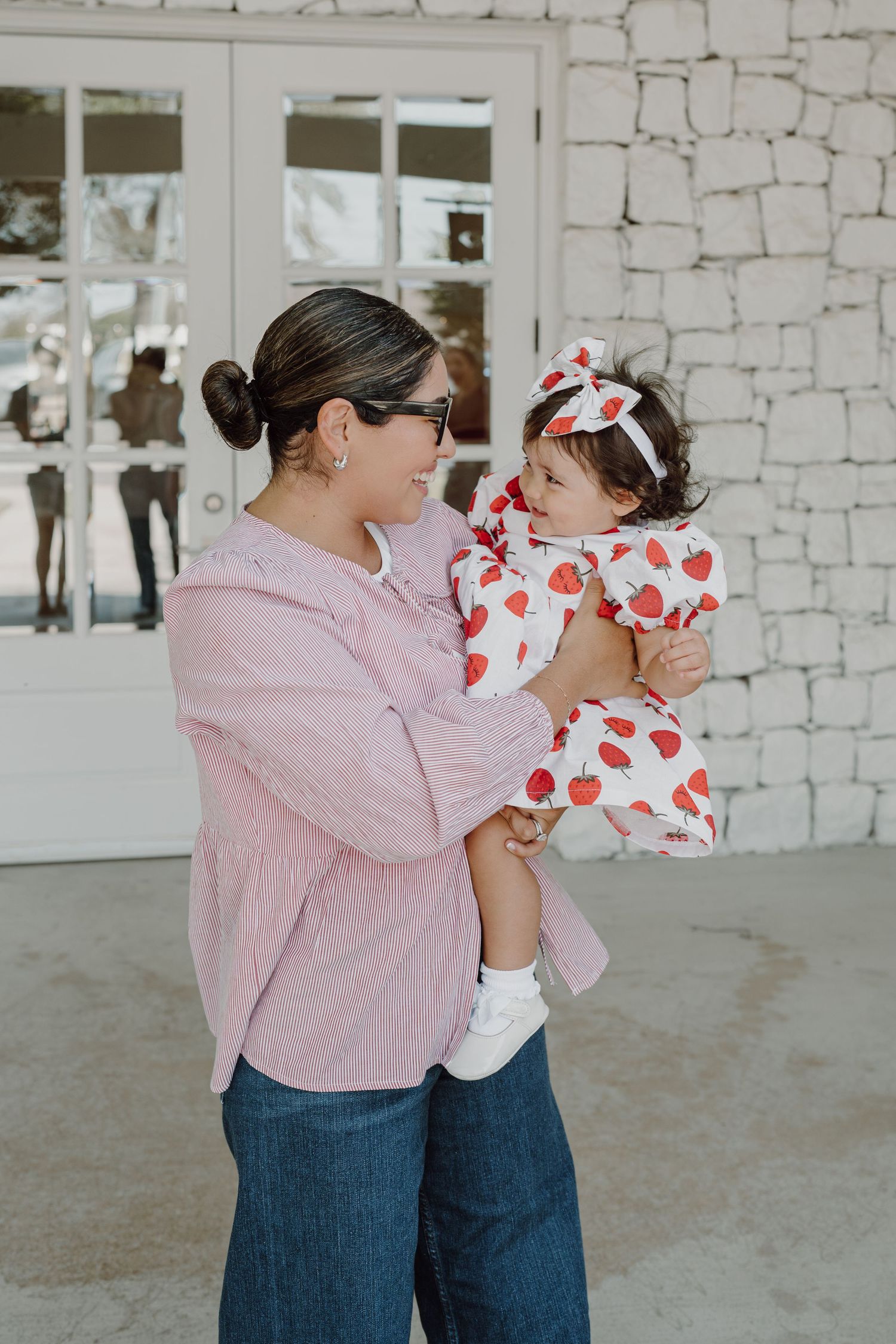 Parent and child in matching pink and heart-patterned outfits pose against white stone wall.
