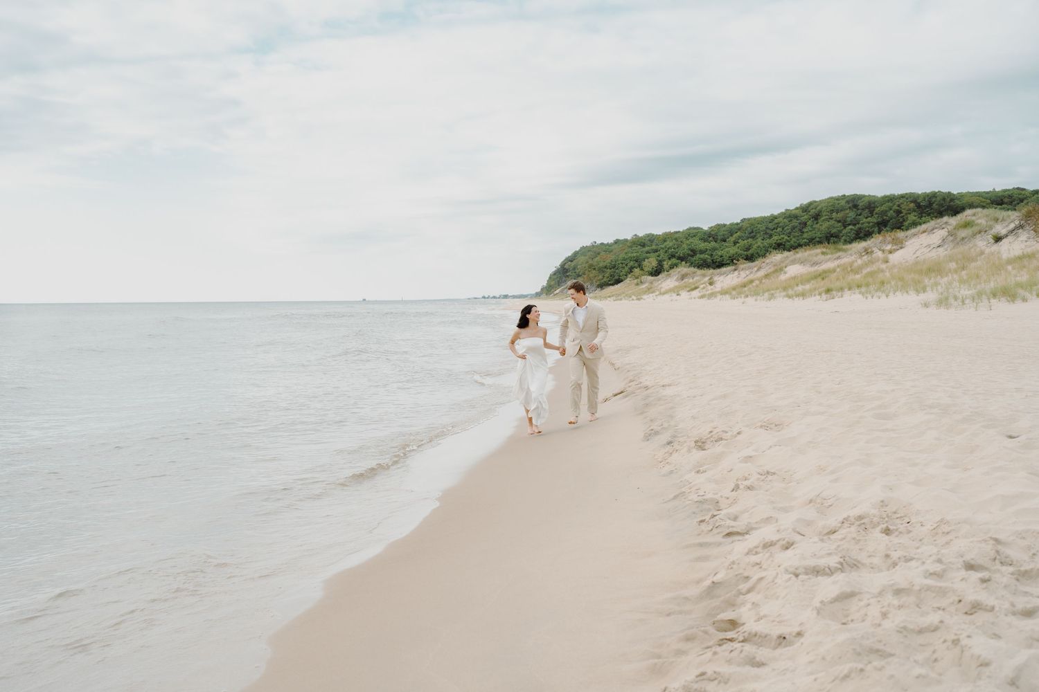 Minimalist beach landscape with figures walking along the sandy shoreline near coastal cliffs.