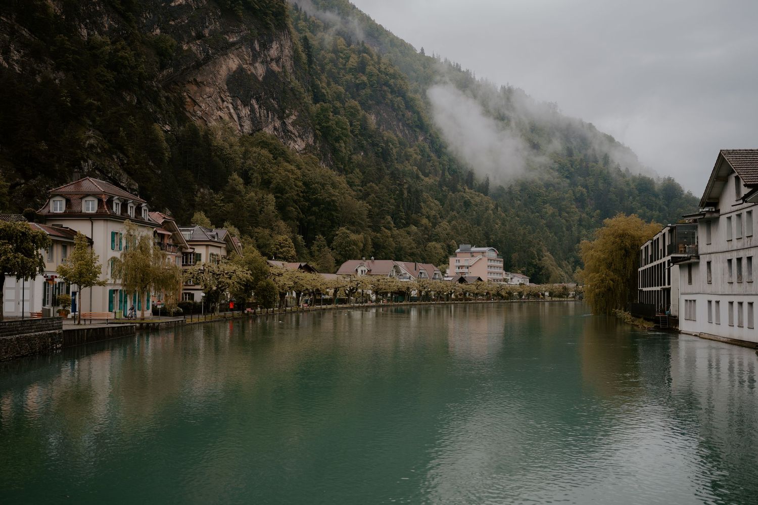Misty mountain lake surrounded by traditional European buildings and autumn foliage.