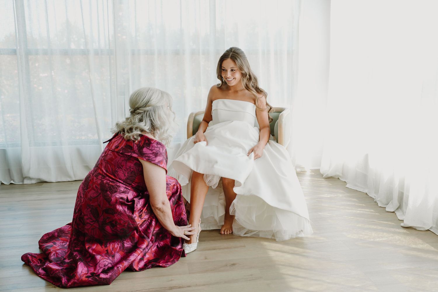 Elegant bridal party wearing burgundy dresses poses in a light-filled room.