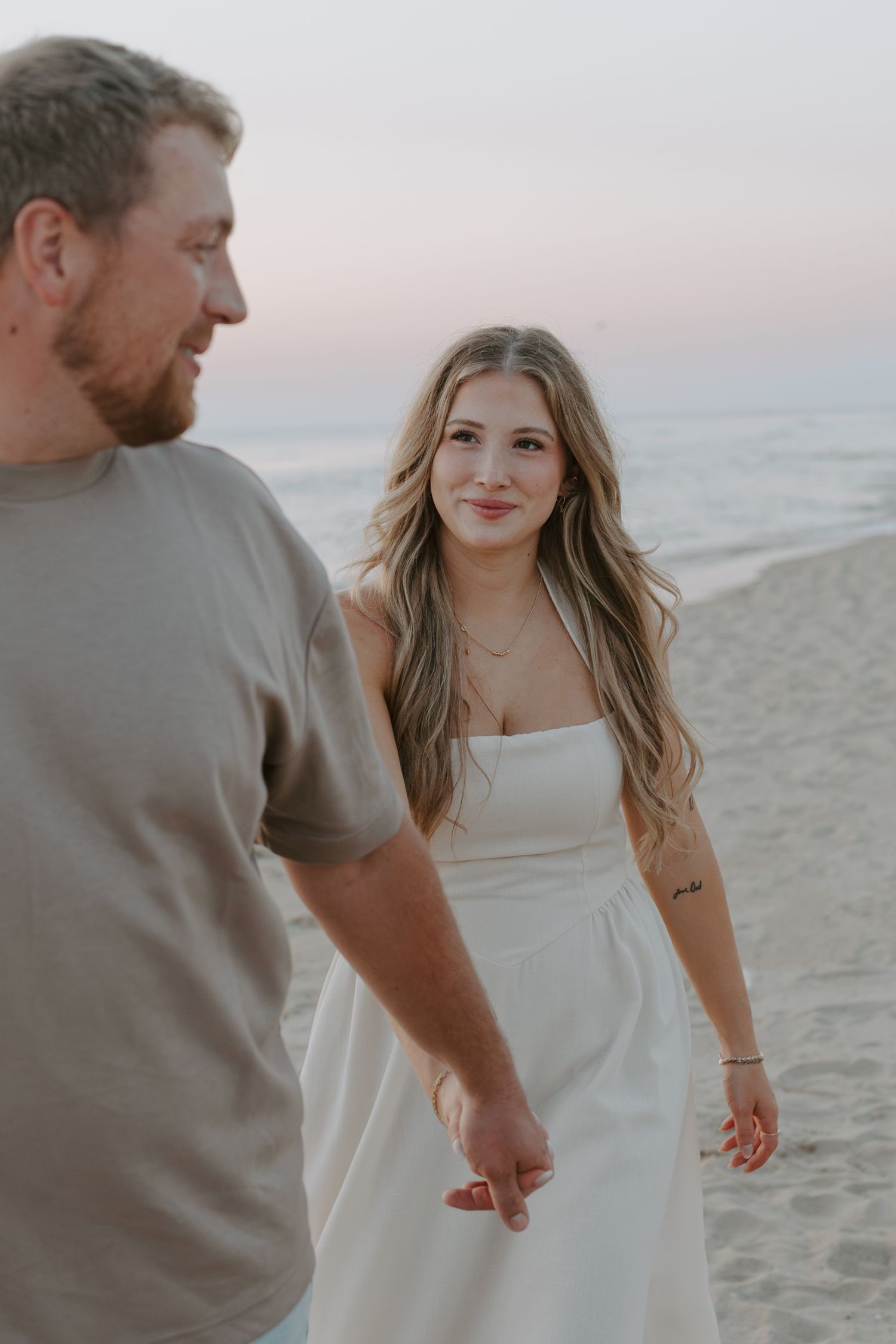 A romantic beach photoshoot featuring a couple in casual attire against a coastal backdrop.