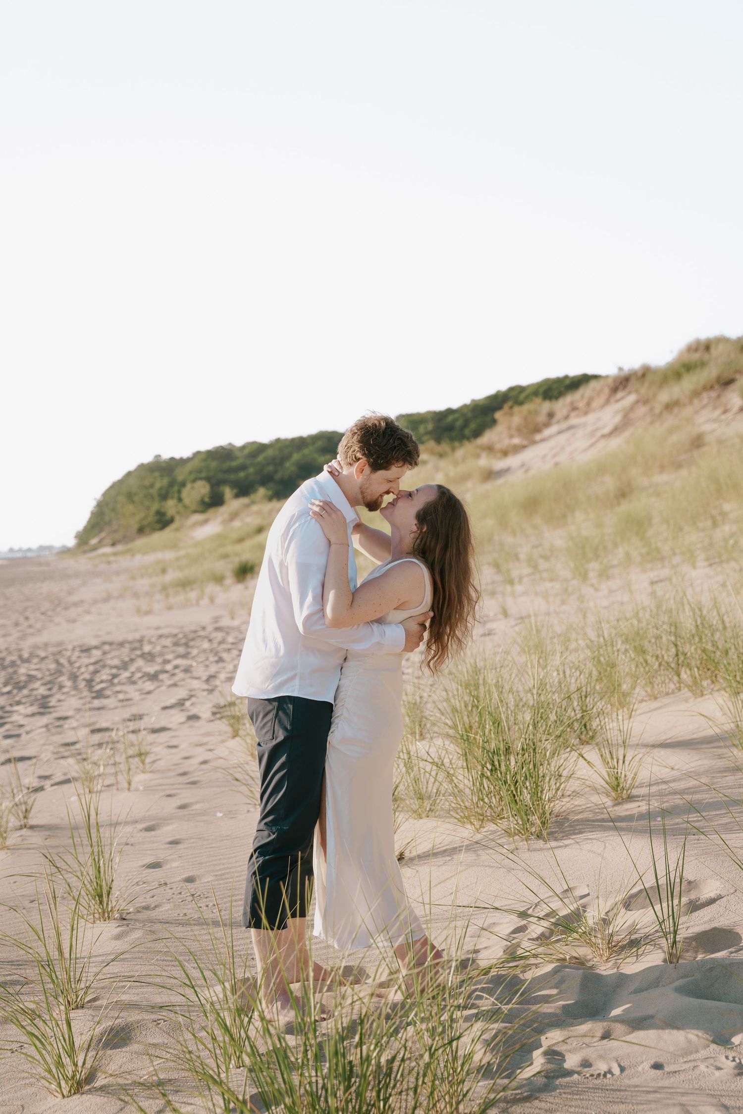 A romantic embrace captured on a scenic beach with sand dunes and beach grass.