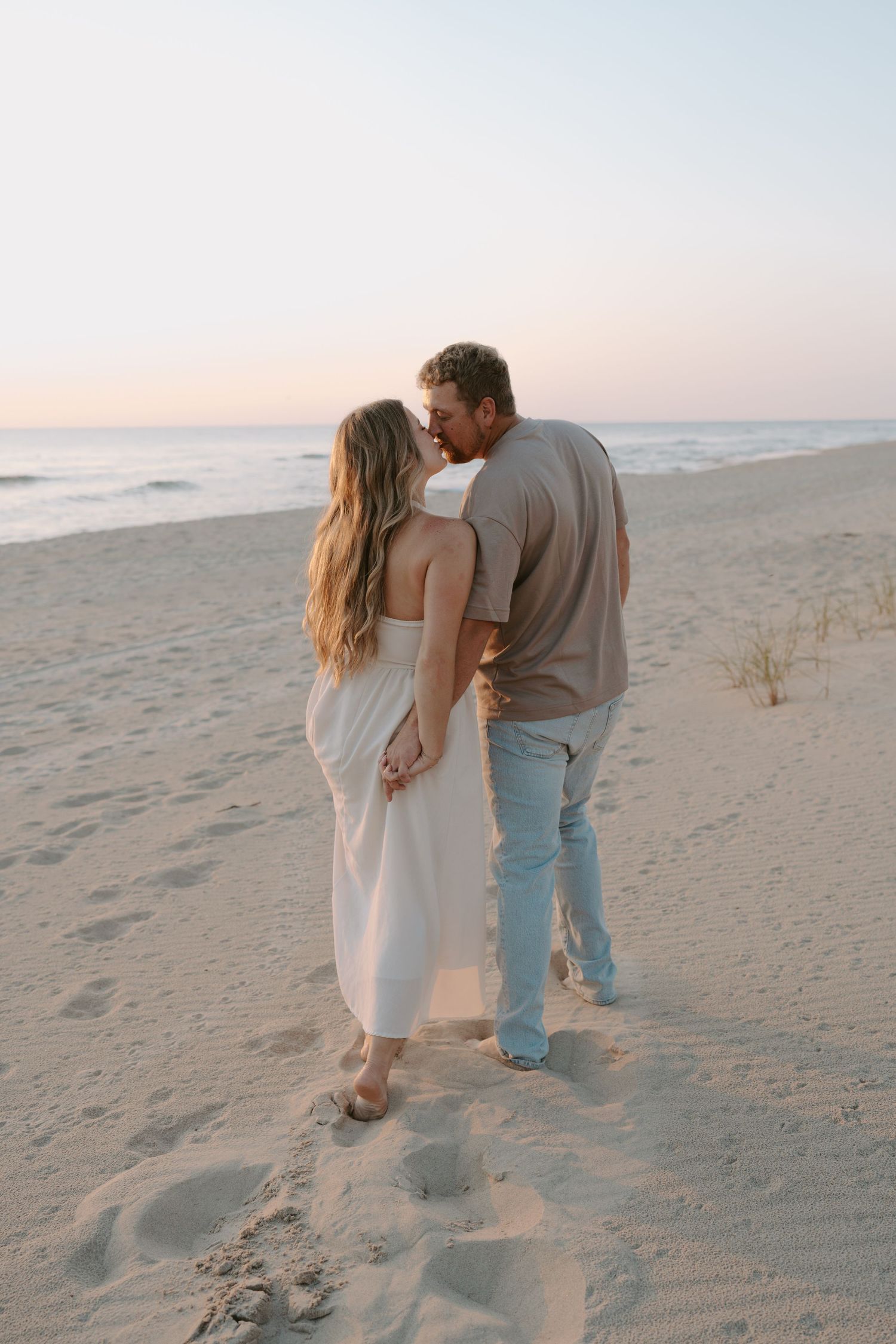 Intimate moment between couple on beach with waves crashing in background.