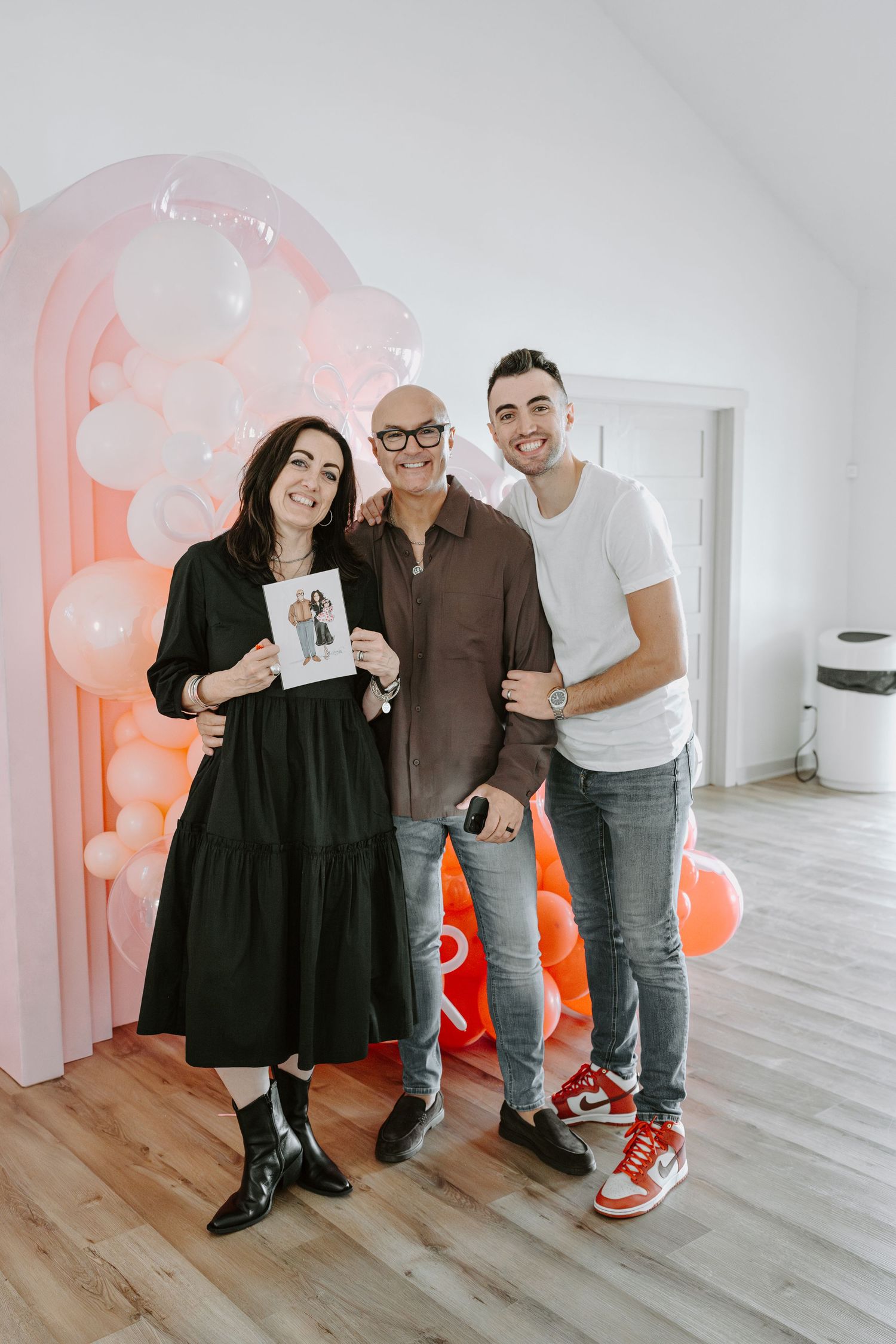 Group posing with photos in modern room decorated with pink and orange balloons.