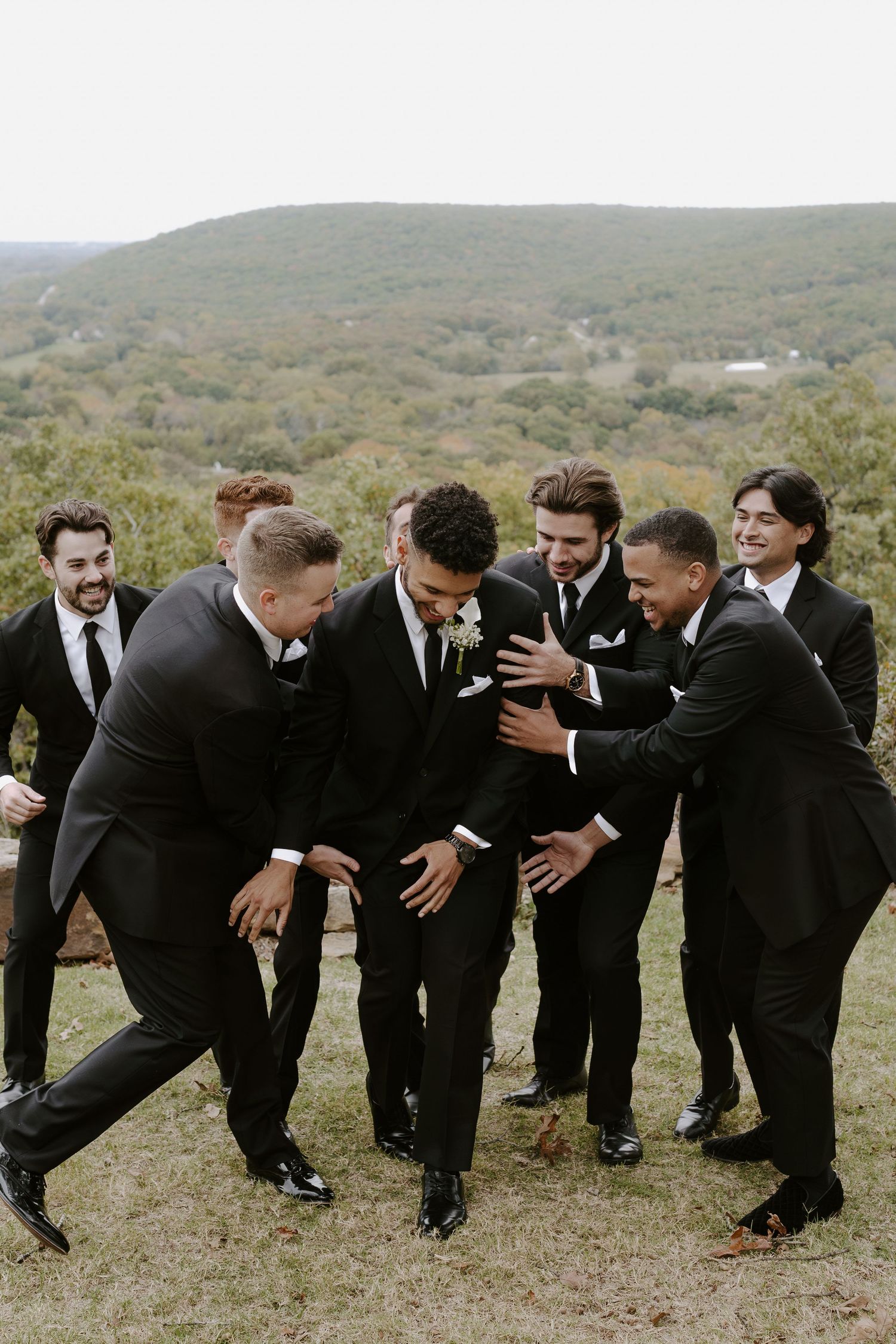 Groomsmen share a candid laughing moment together on a scenic overlook.