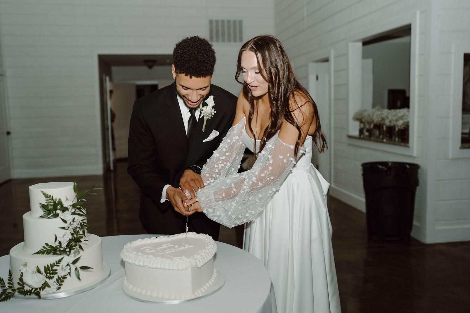 Newlyweds slice into their white wedding cake during the reception.