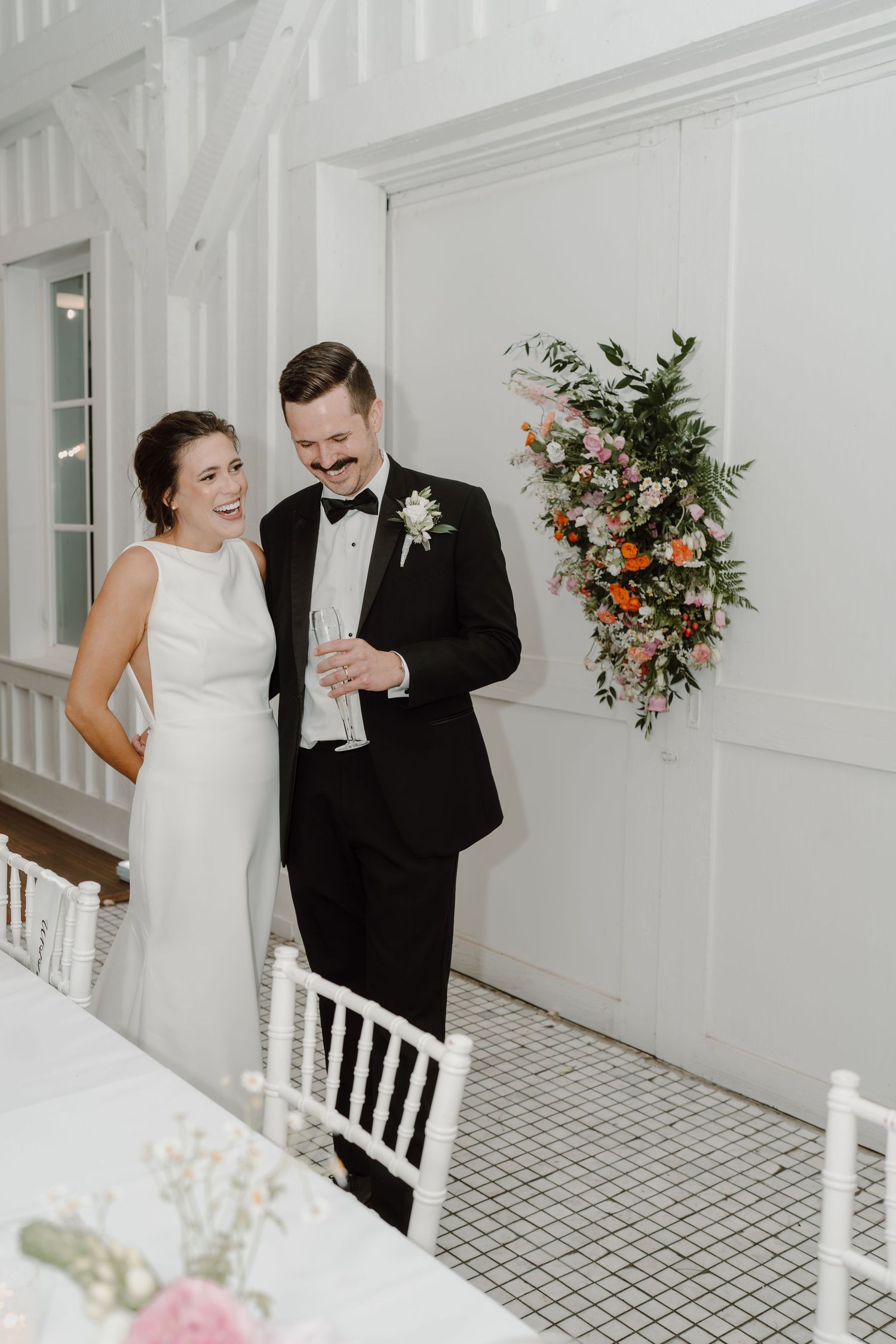Wedding celebration unfolds in a bright white venue with elegant floral arrangements.