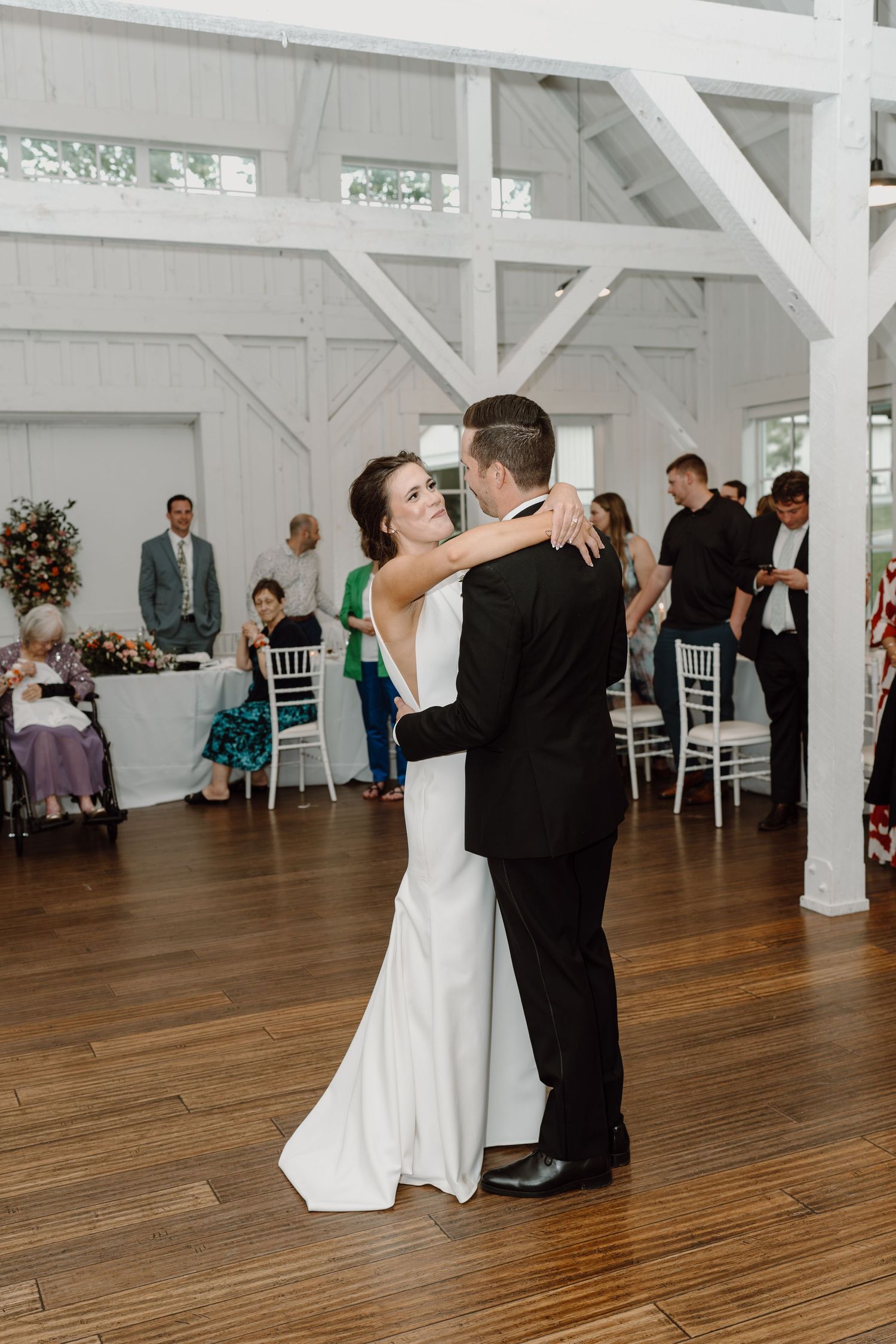 Newlyweds sharing an intimate dance moment on wooden floors in a bright white reception venue.