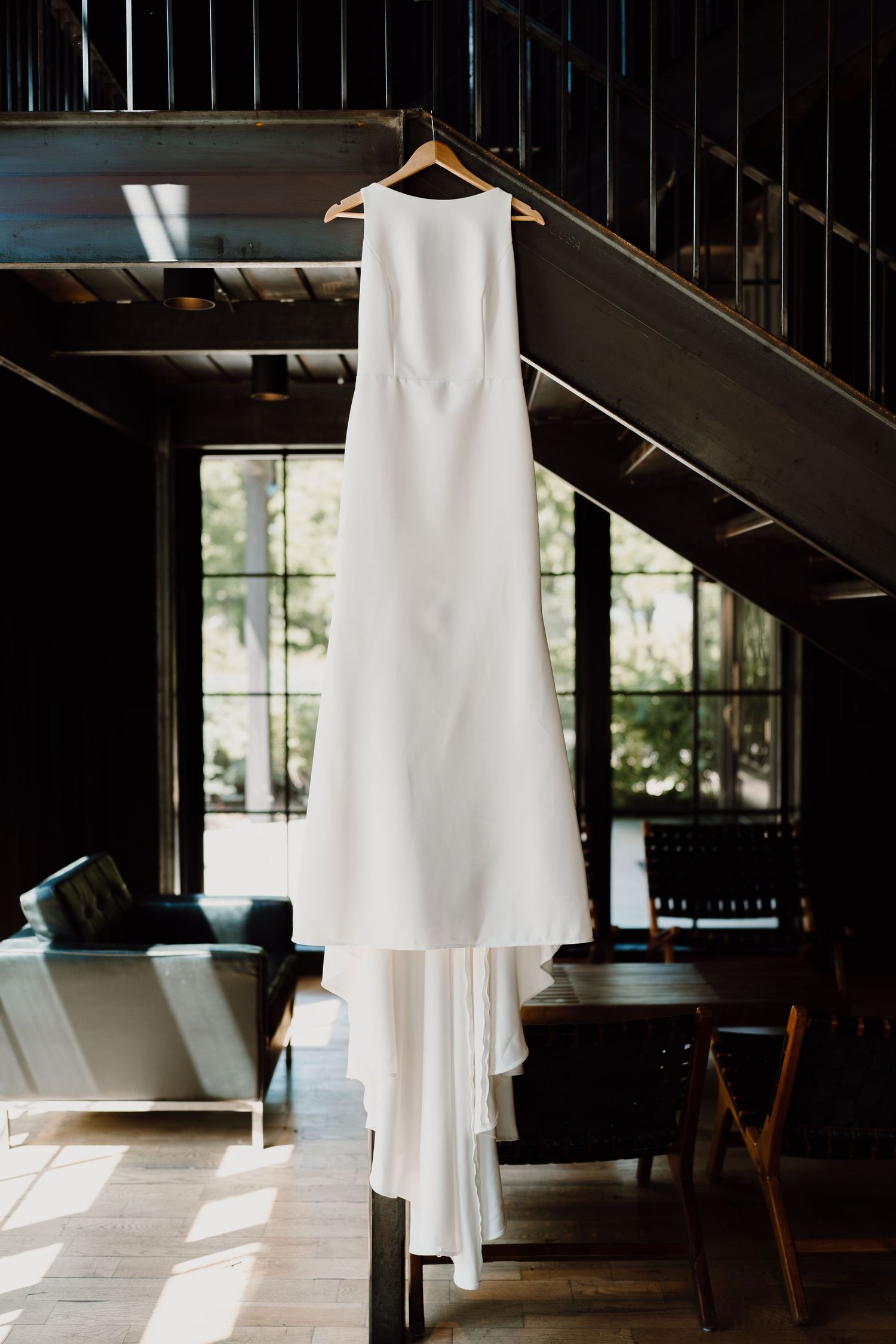 White wedding dress hanging in dramatic lighting against dark interior.