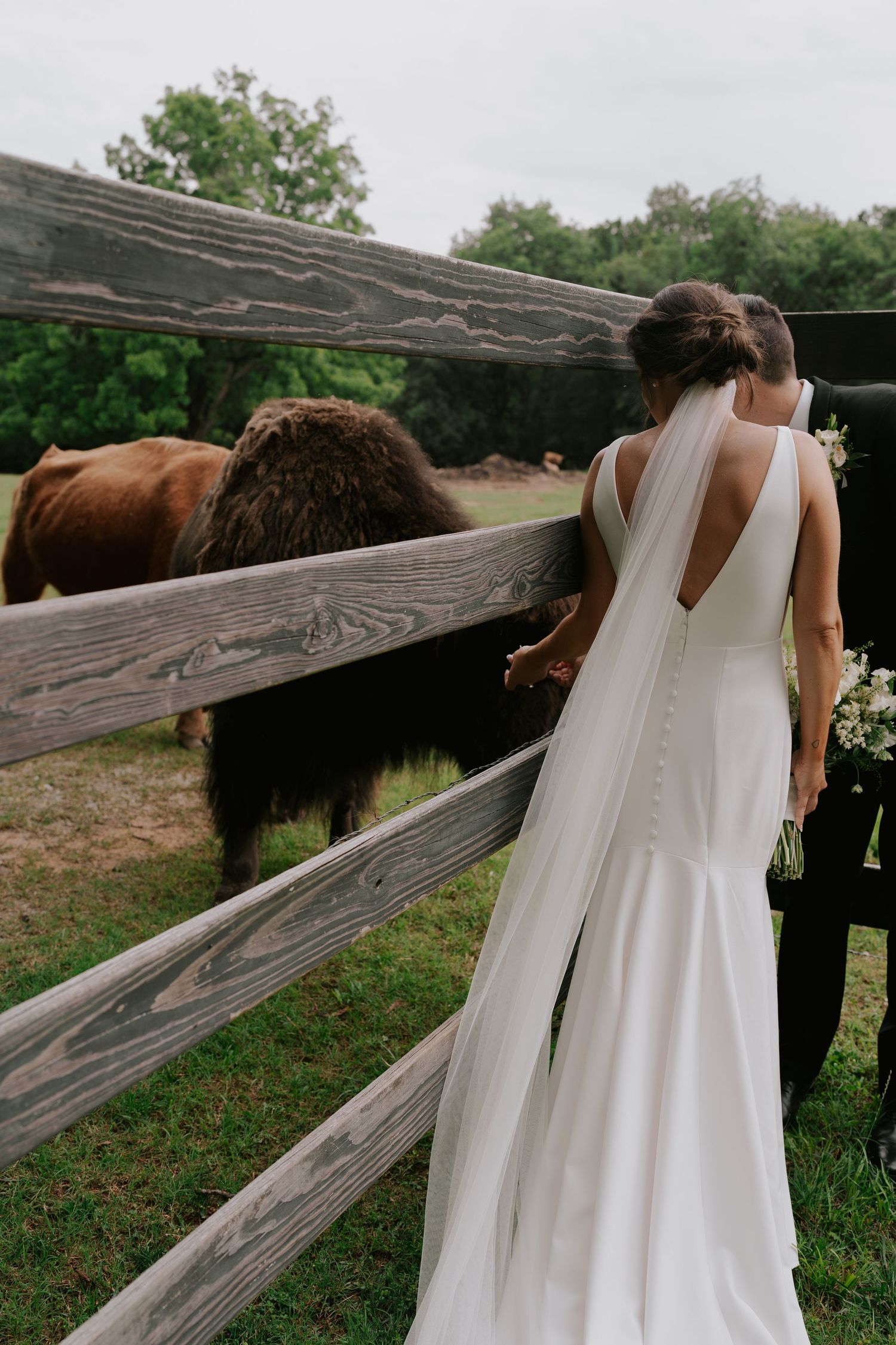 White wedding dress flowing against weathered wooden fence posts in a rustic outdoor setting.