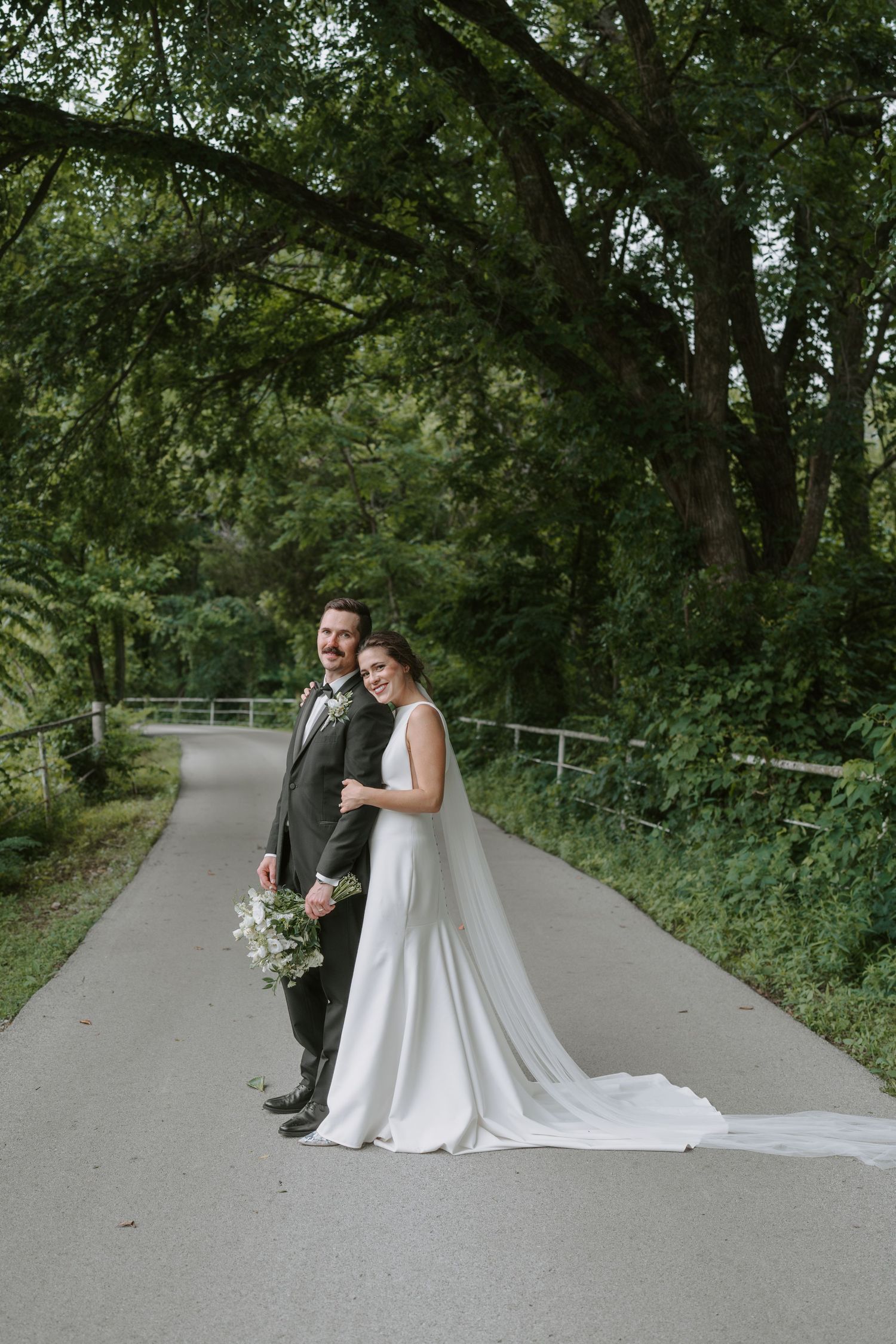 Romantic wedding photo showing a couple embracing on a peaceful tree-lined pathway.