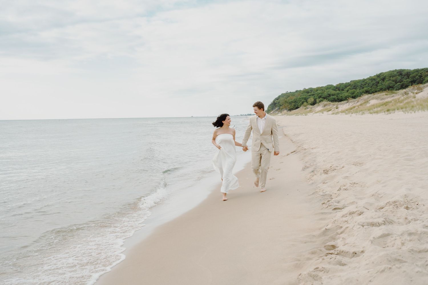 Wide angle beach scene with distant figures walking along the shoreline near vegetated cliffs.