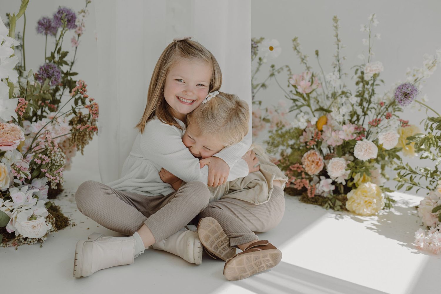 Tender sibling embrace captured in natural light with romantic floral backdrop.