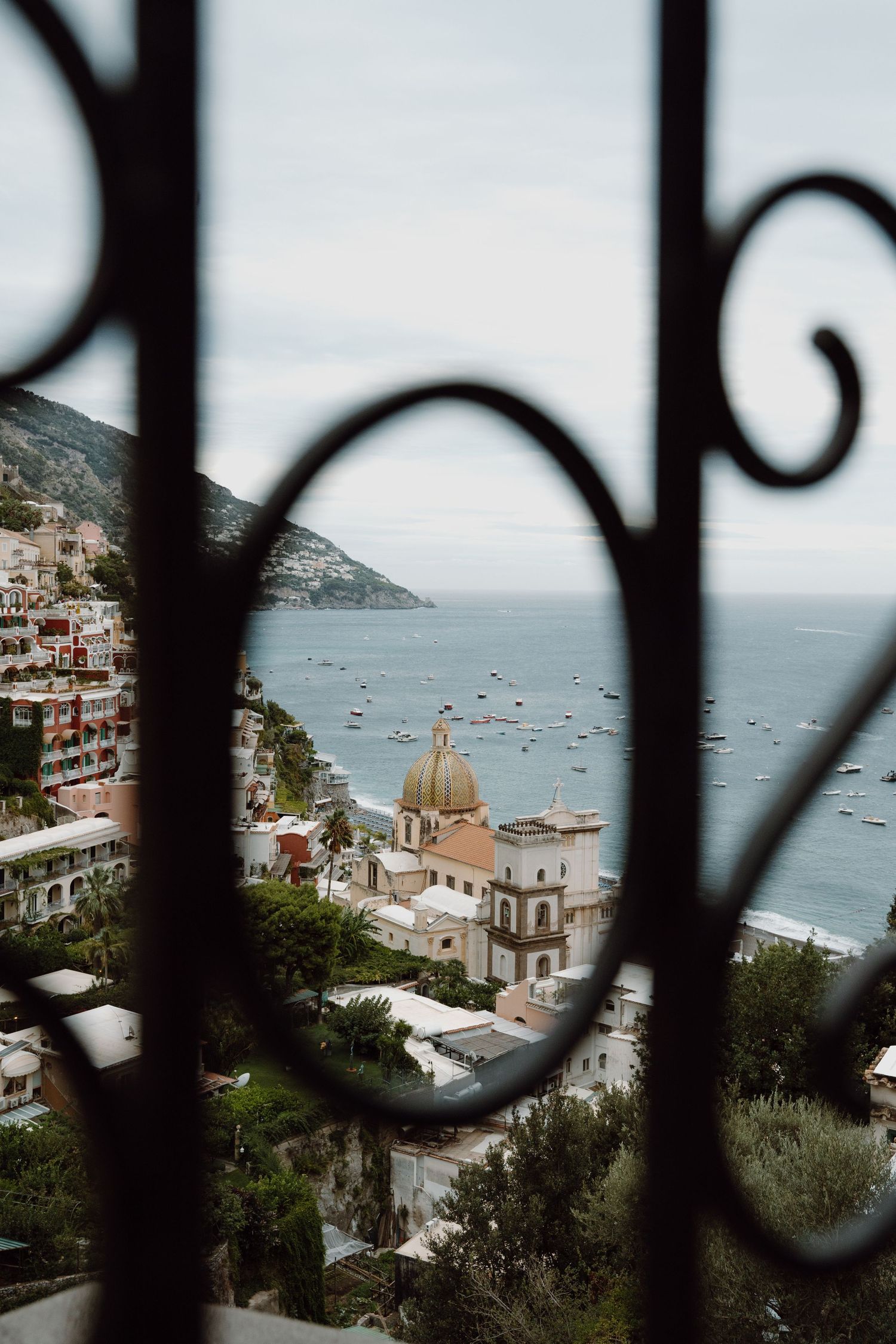 Coastal Mediterranean town with church dome viewed through decorative iron railings.
