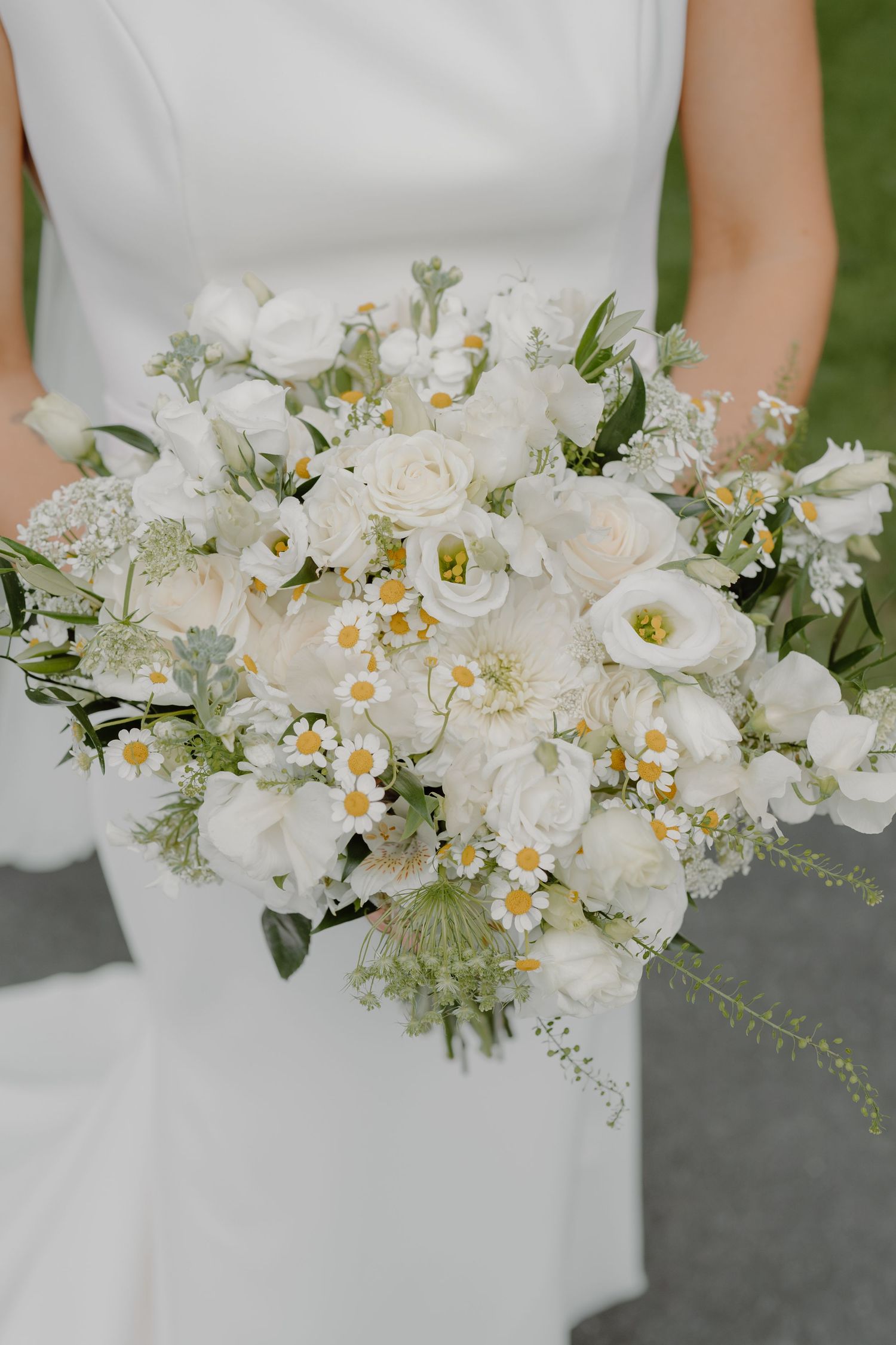 A stunning white wedding bouquet with daisies and delicate flowers against a white dress.