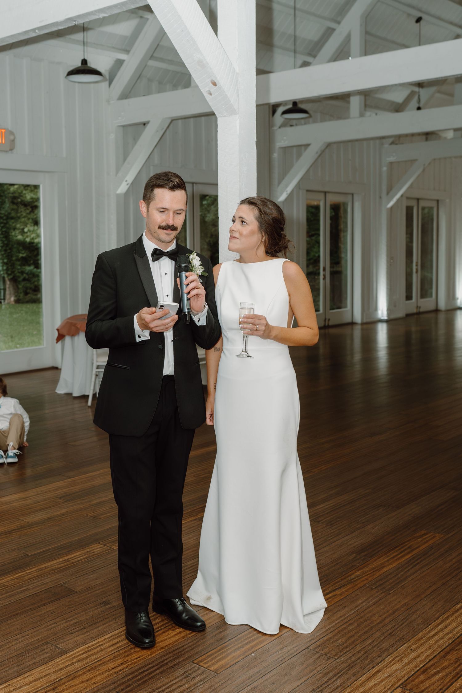 Couple sharing drinks and smiles in an elegant white barn wedding venue.
