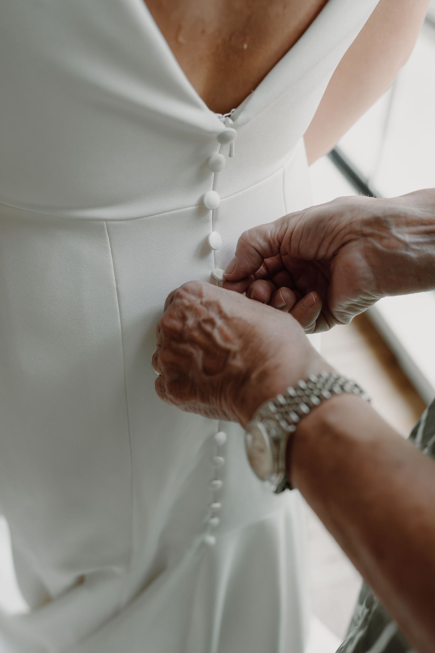 Close-up of hands buttoning up the back of an elegant white wedding dress.