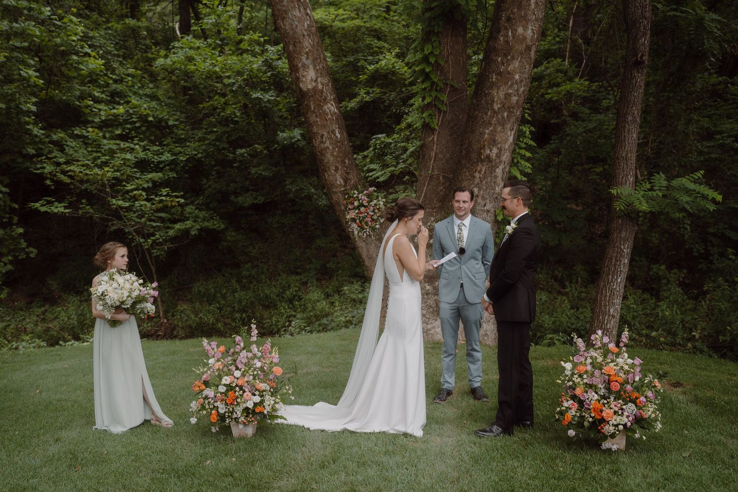 Wedding ceremony in progress surrounded by trees and vibrant floral decorations.