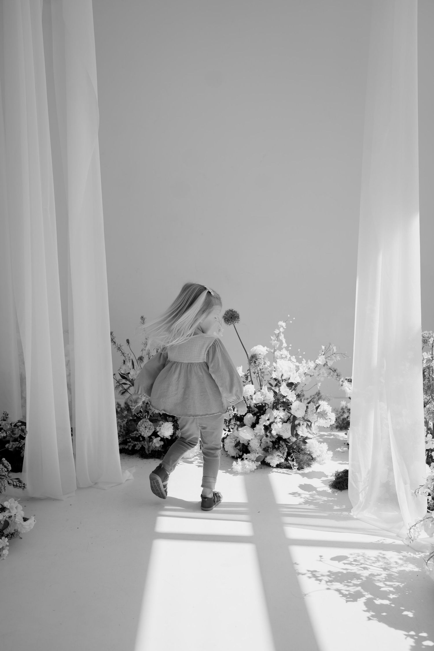 Clean white studio space with elegant floral displays and draped fabric casting artistic shadows.