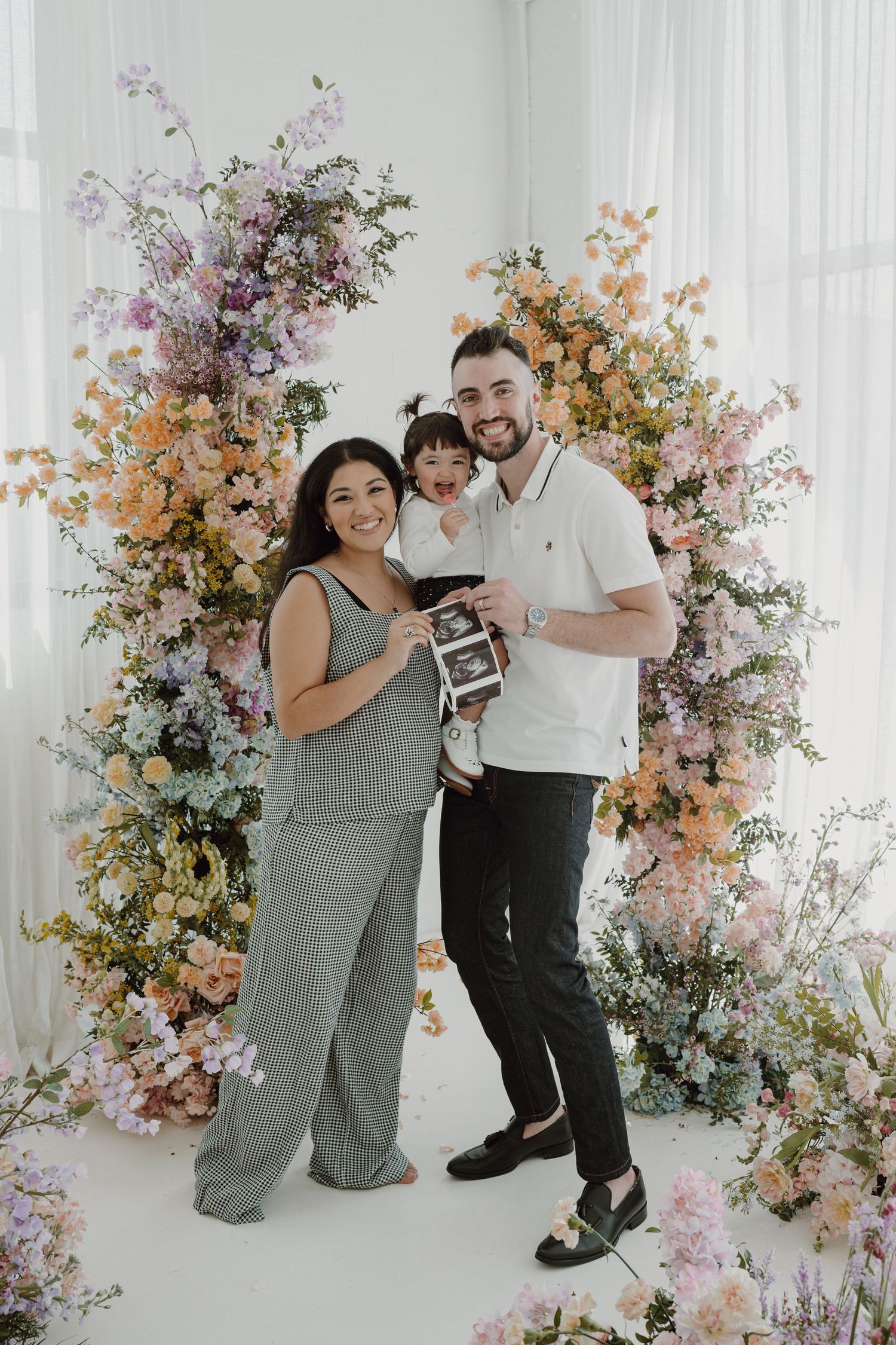 Family poses with ultrasound photos during spring-themed pregnancy announcement session.