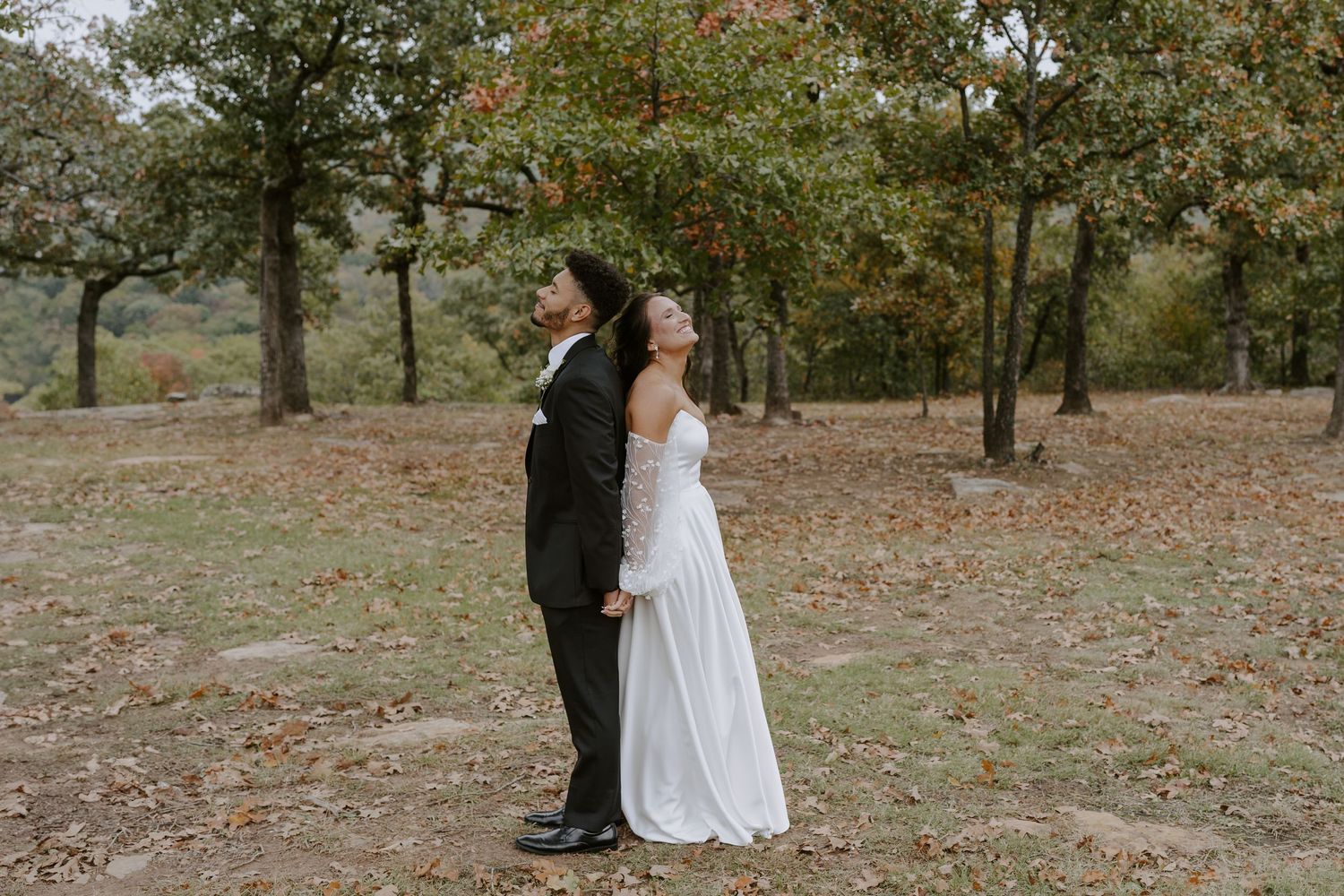 A wedding couple stands together among fall trees during their outdoor photo session.