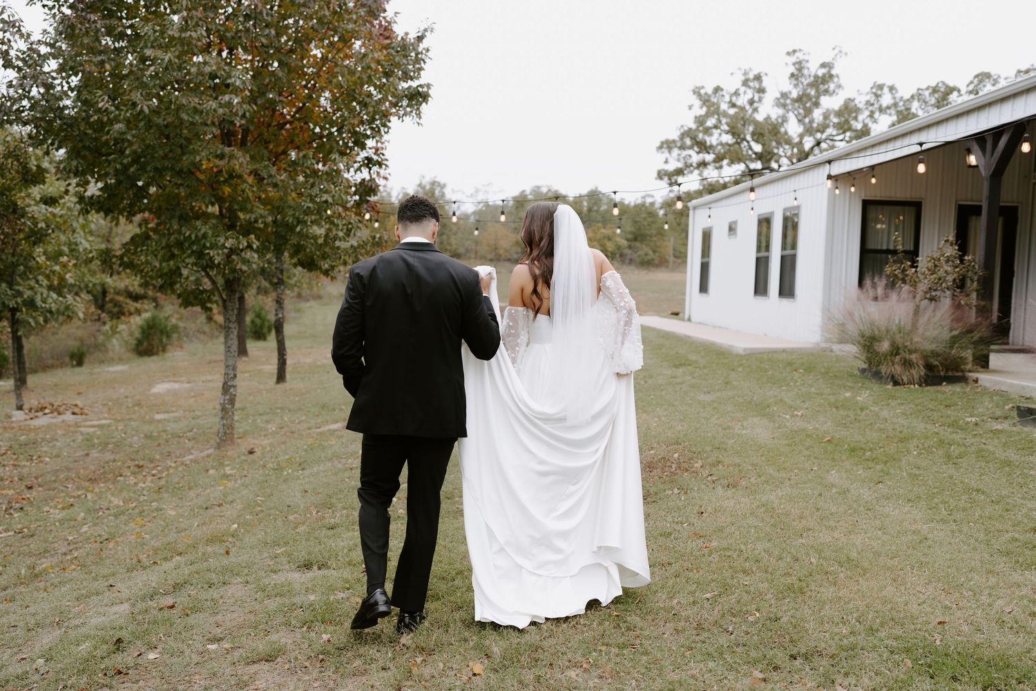 A couple walks along a path near a white building surrounded by autumn trees.