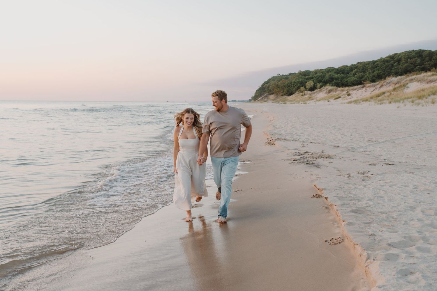 Casual beach walk along the water's edge with dunes in the background.