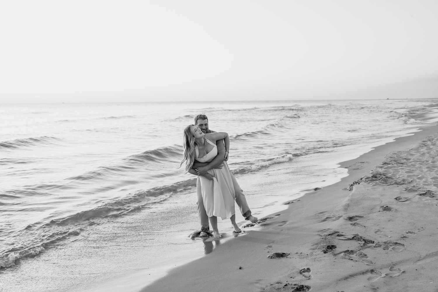 Two people enjoying a romantic walk on a black and white beach with waves crashing nearby.