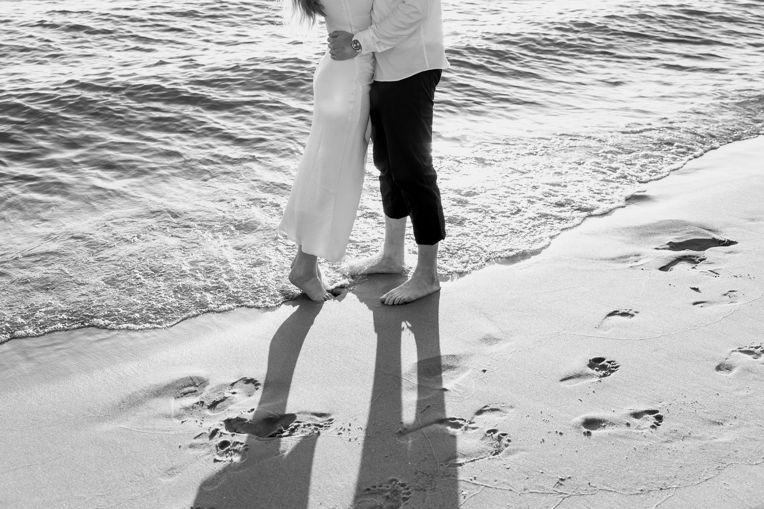 Feet and shadows of a couple standing together on wet beach sand.
