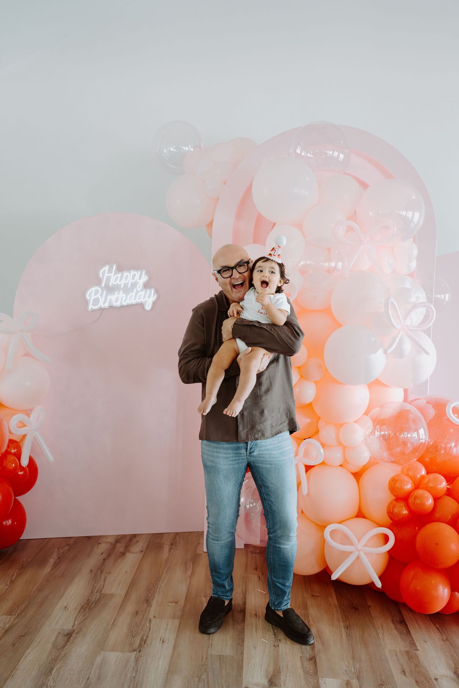 A joyful moment captured with a baby in front of a birthday balloon display.